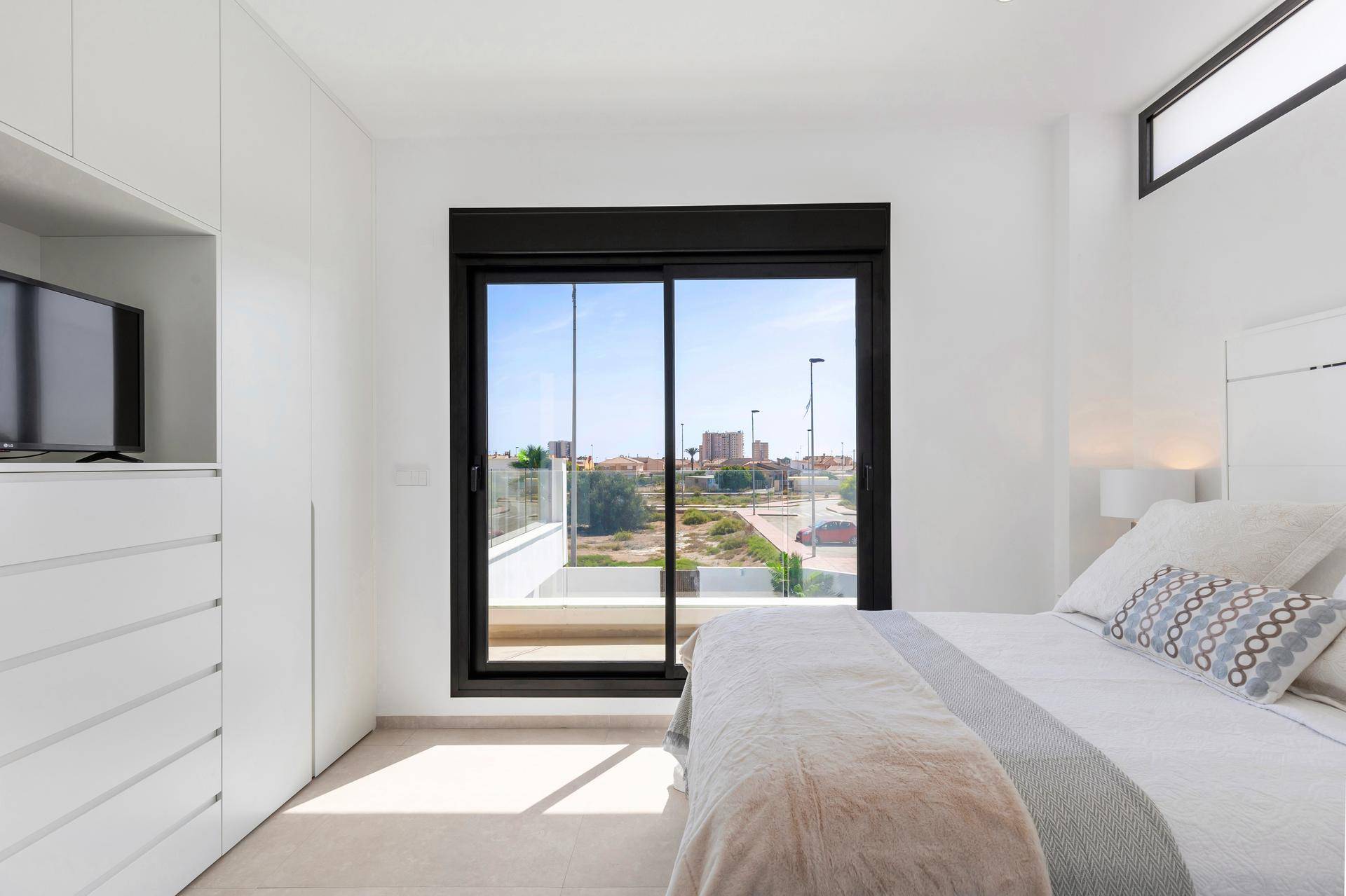 Helles Schlafzimmer mit großem Fenster, Einbauschränken und Blick auf die Umgebung.