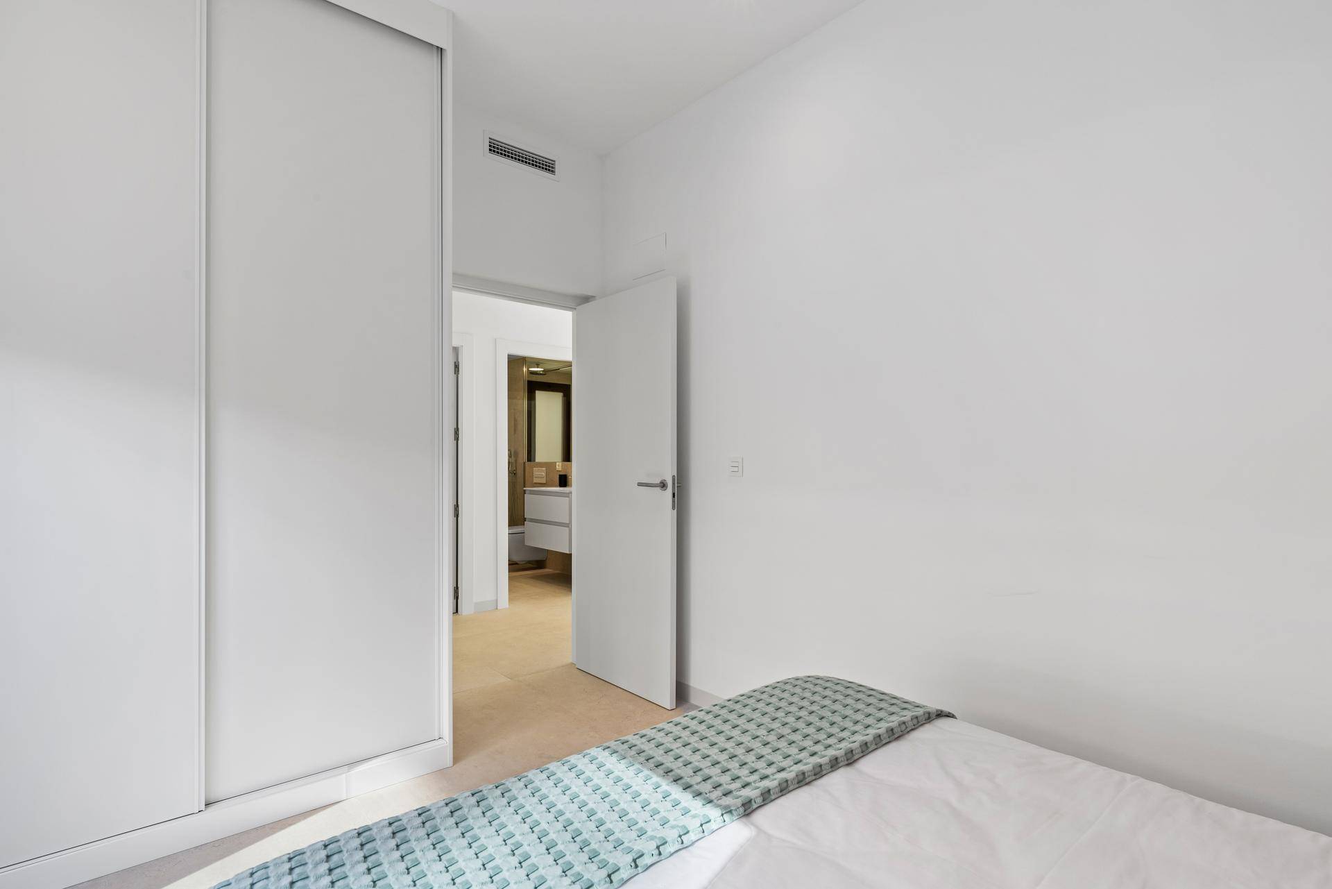 Modernes Schlafzimmer mit weißem Einbauschrank und direktem Zugang zu einem stilvollen Badezimmer.