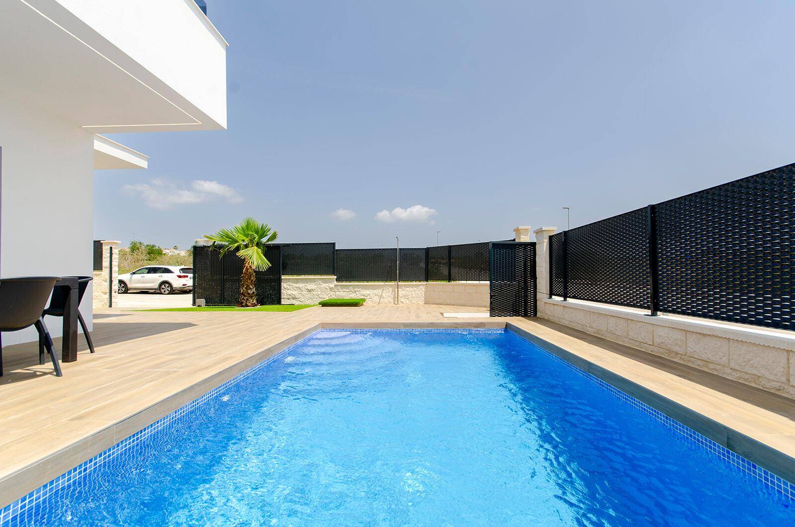 Langer, rechteckiger Pool mit blauen Mosaikfliesen und umzäuntem Außenbereich.