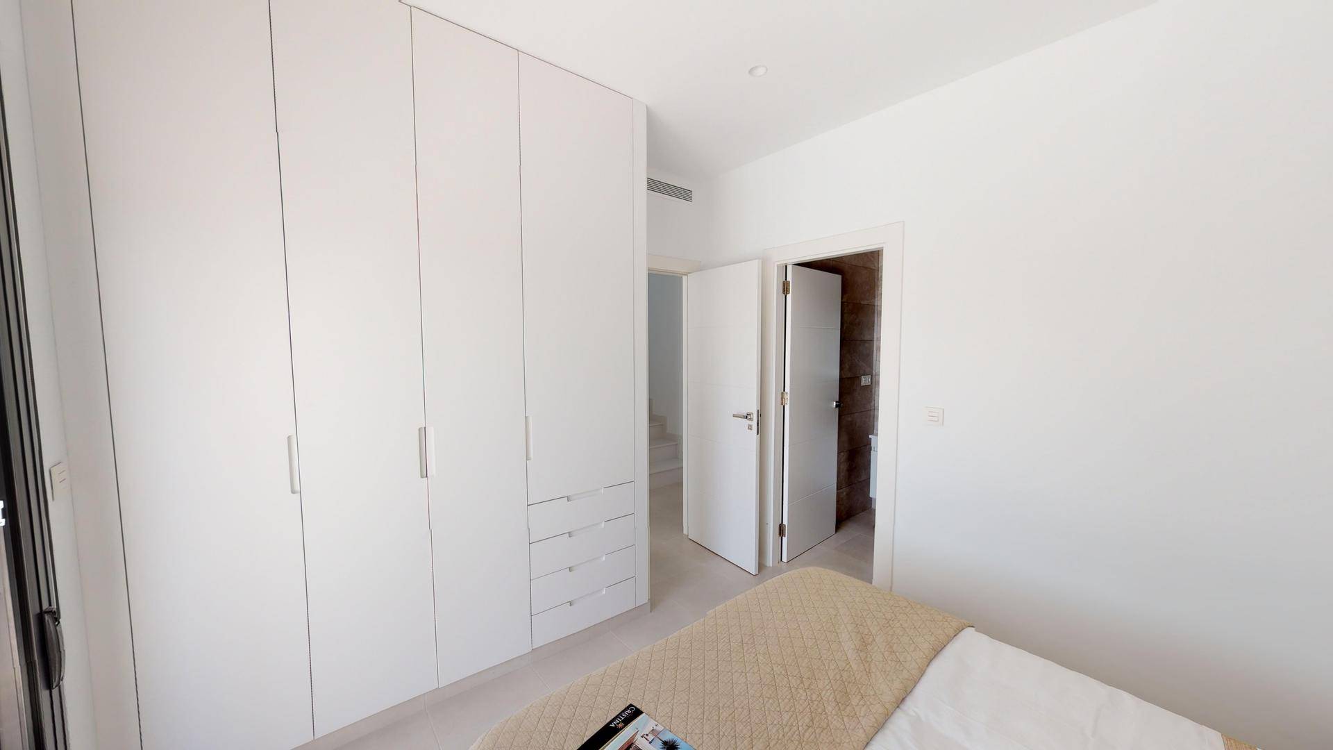 Helles Schlafzimmer mit integrierten weißen Kleiderschränken und Zugang zu einem weiteren Raum.