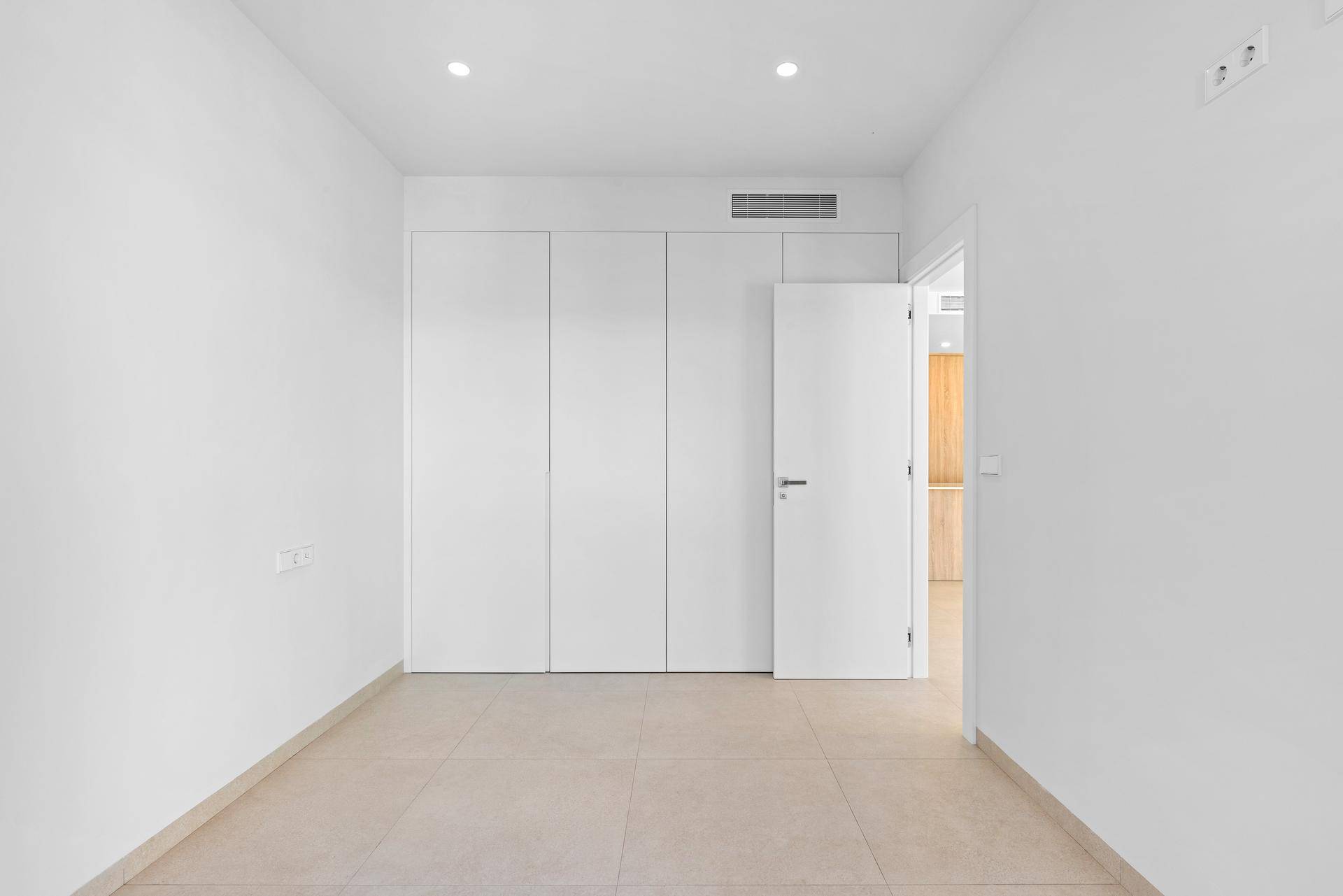 Helles Schlafzimmer mit integrierten weißen Einbauschränken, Fliesenboden und Klimaanlage.