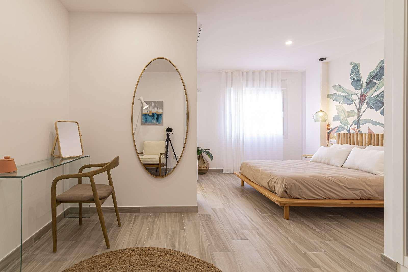 Helles Schlafzimmer mit Holzbett, großem Spiegel und farbenfroher Wanddekoration.