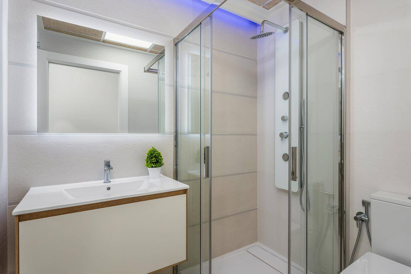 Modernes Badezimmer mit Duschkabine, Einzelwaschbecken und beleuchtetem Spiegel.