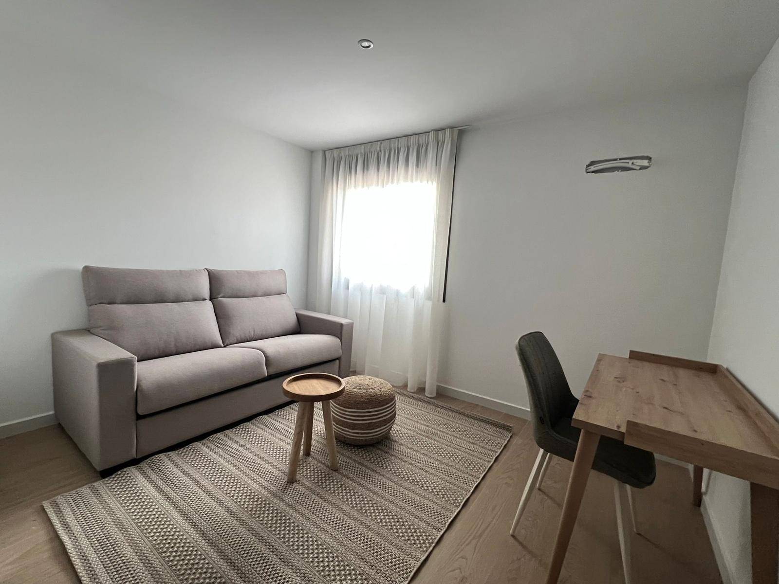 Helles Arbeitszimmer mit Schlafsofa, Schreibtisch und Fenster mit Vorhängen.