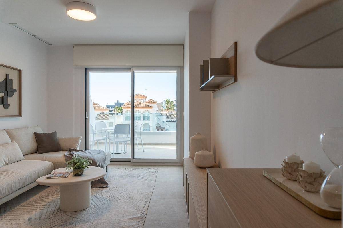 Modern eingerichtetes Wohnzimmer mit beigem Sofa, Couchtisch und Zugang zum Balkon.