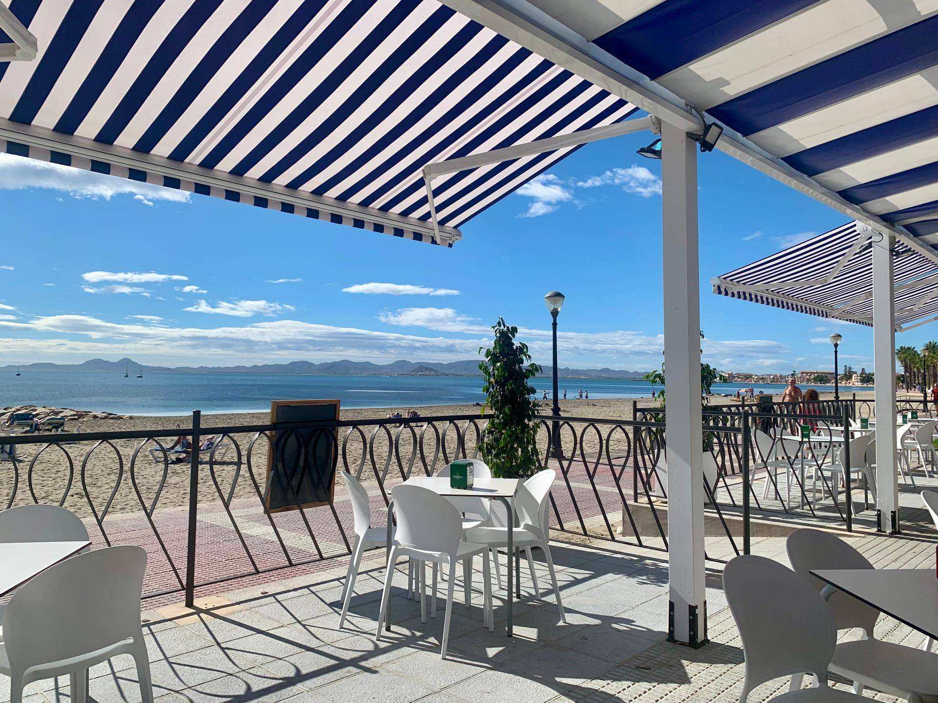 Strandcafé mit gestreiften Markisen, Tischen und Stühlen direkt am Meer.