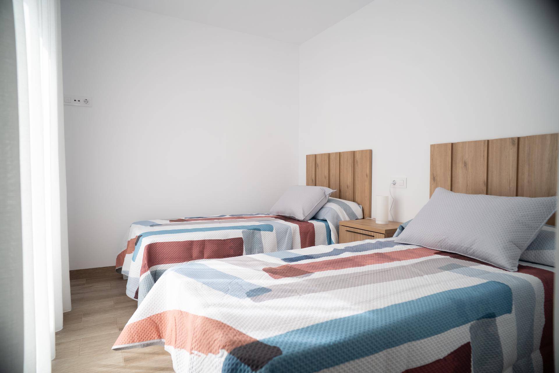 Helles Schlafzimmer mit zwei Einzelbetten, Holzkopfteilen und modernem Laminatboden.