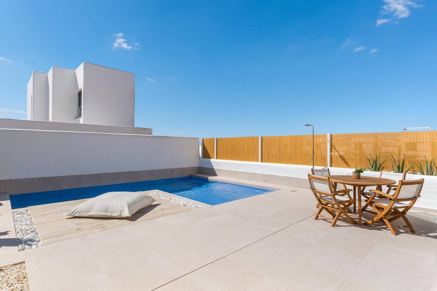 Sonniger Außenbereich mit Pool, gefliester Terrasse und Essbereich im Freien.