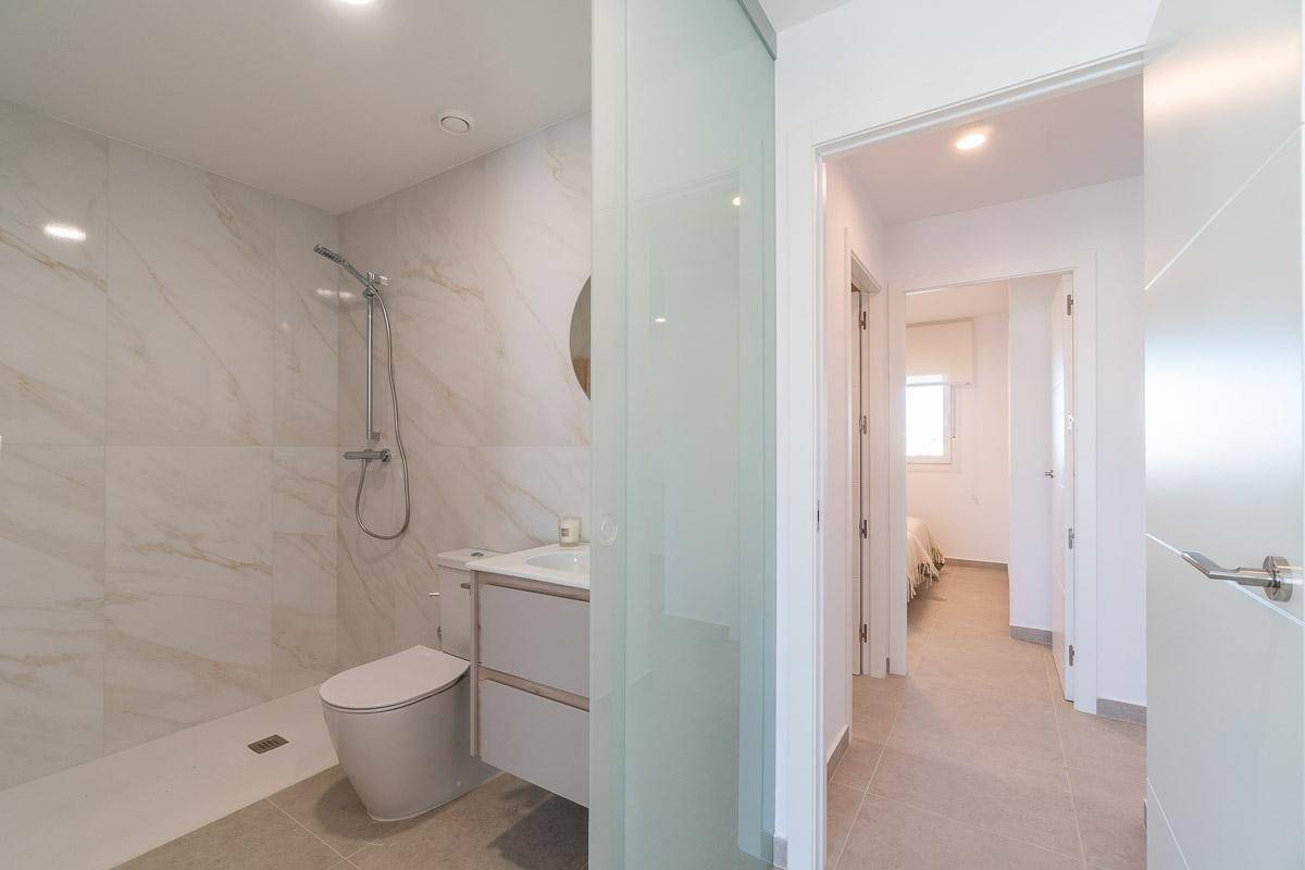 Modernes Badezimmer mit Marmoroptik-Fliesen, ebenerdiger Dusche und Glasschiebetür.