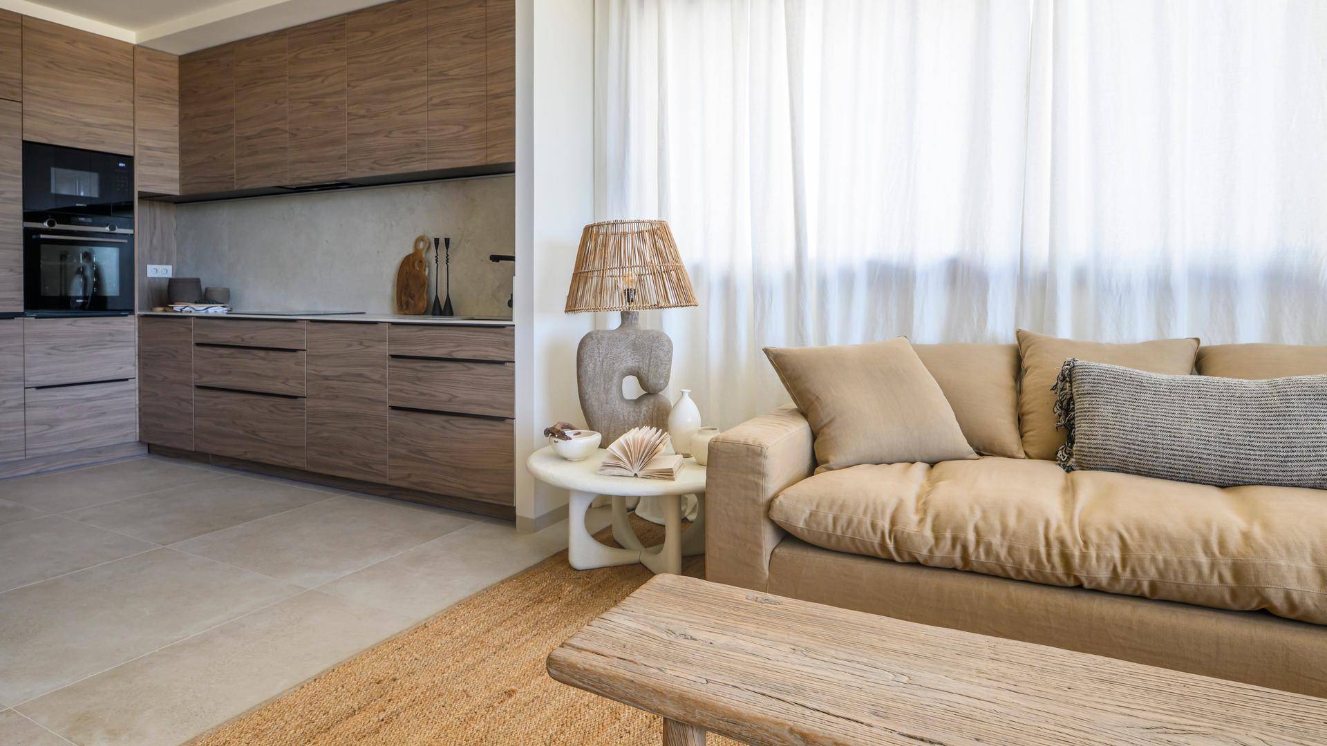 Heller Wohnbereich mit beigem Sofa, Beistelltisch und dekorativer Lampe, mit Blick auf die moderne Küche.
