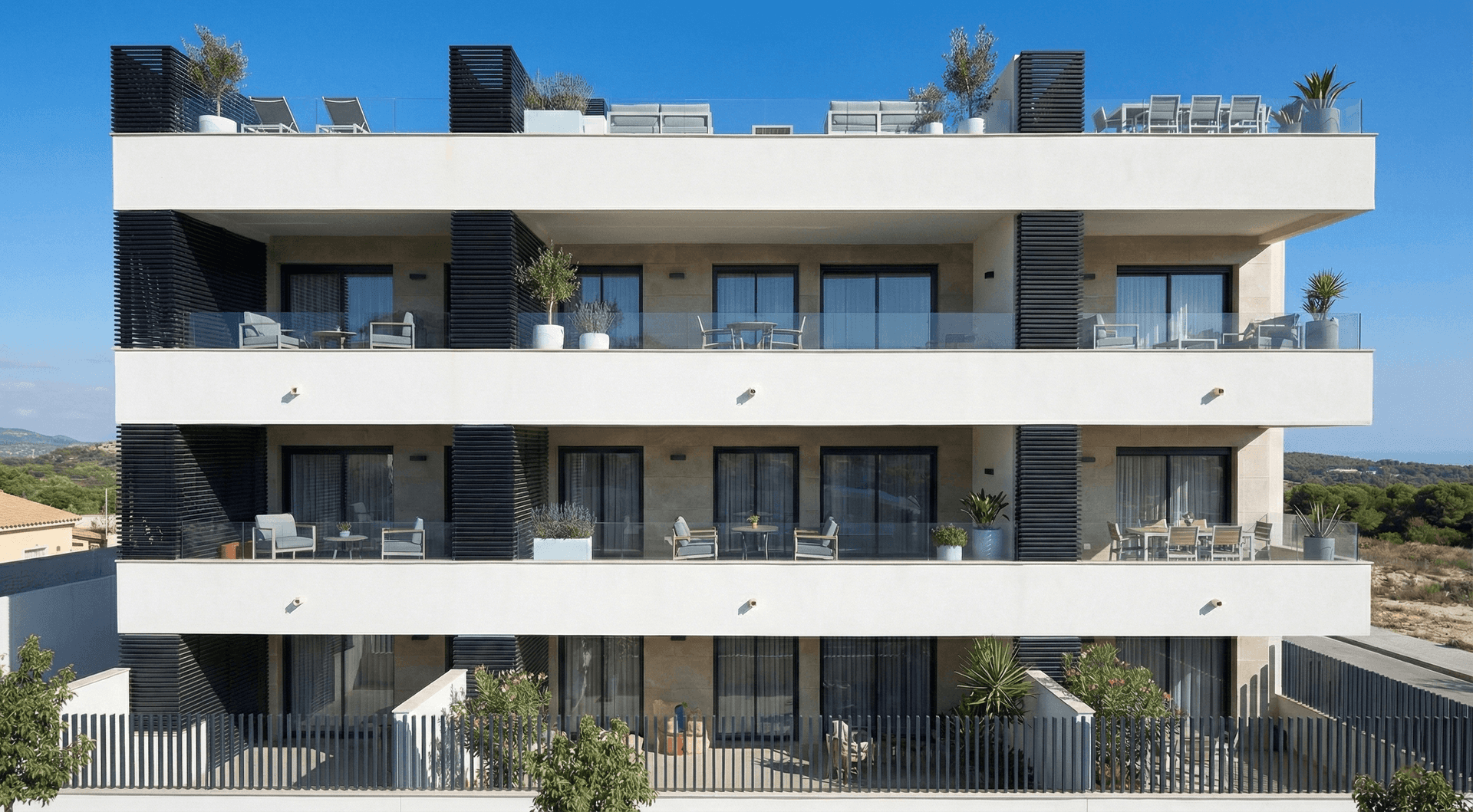 Moderne Fassade eines Apartmentgebäudes mit großzügigen Balkonen und Dachterrassen unter blauem Himmel.