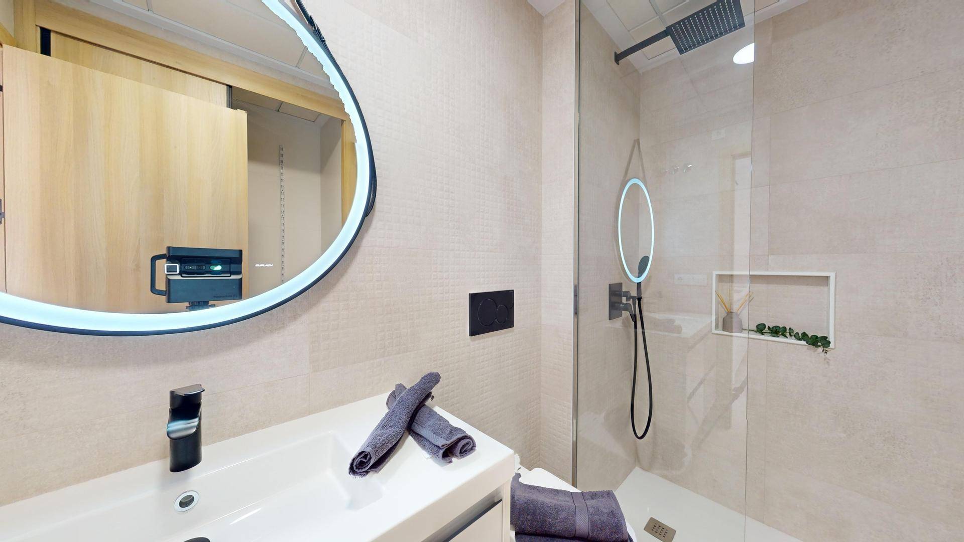 Helles Badezimmer mit modernem Waschtisch, beleuchtetem Spiegel und begehbarer Dusche.