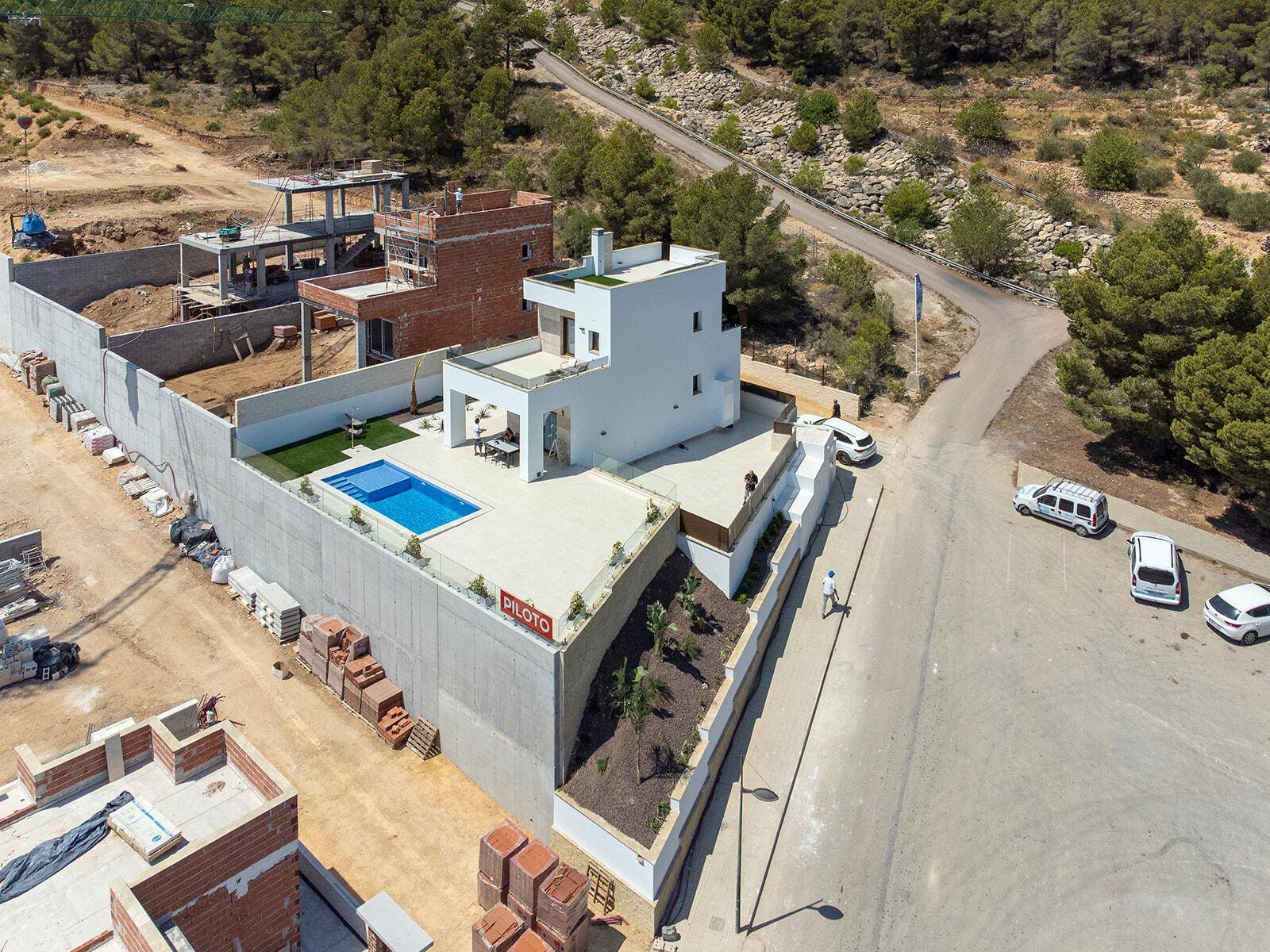 Luftaufnahme einer modernen Villa mit Pool und umliegenden Baustellen in hügeliger Landschaft.