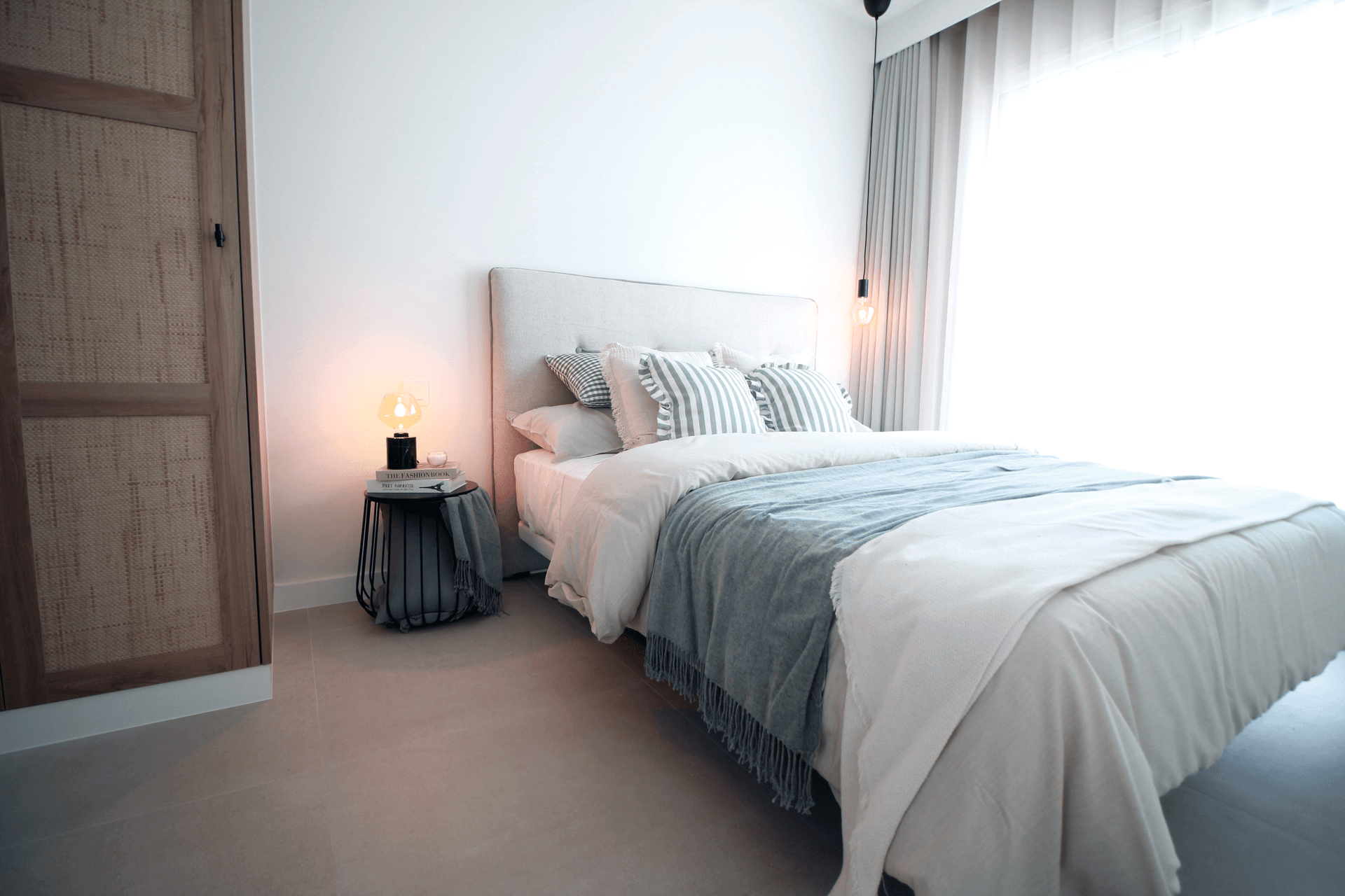 Helles Schlafzimmer mit Doppelbett, Rattanschränken und Zugang zu einem Fenster mit Vorhängen.