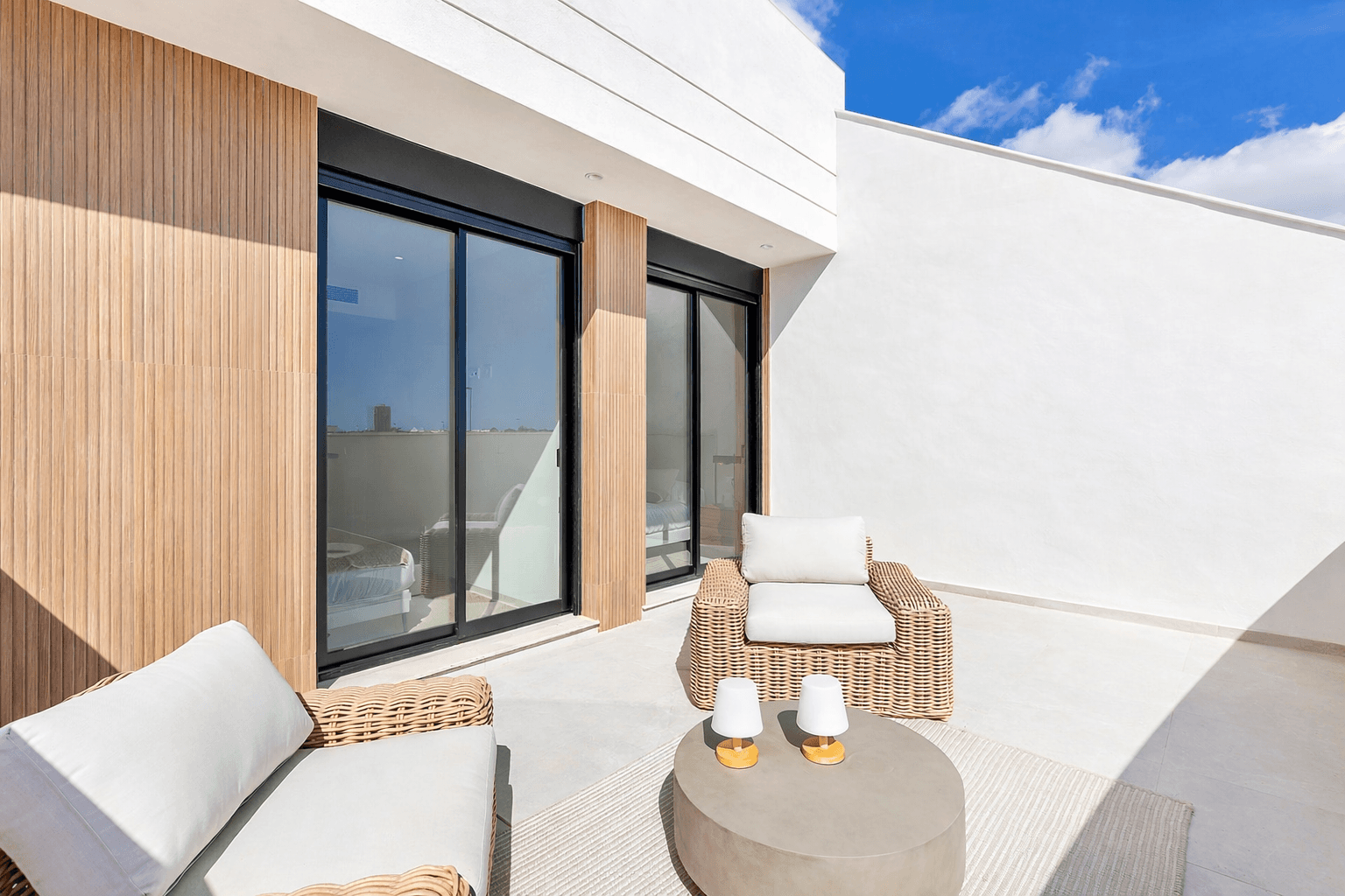 Sonnige Dachterrasse mit bequemen Korbsesseln und Holzakzenten an der Fassade.