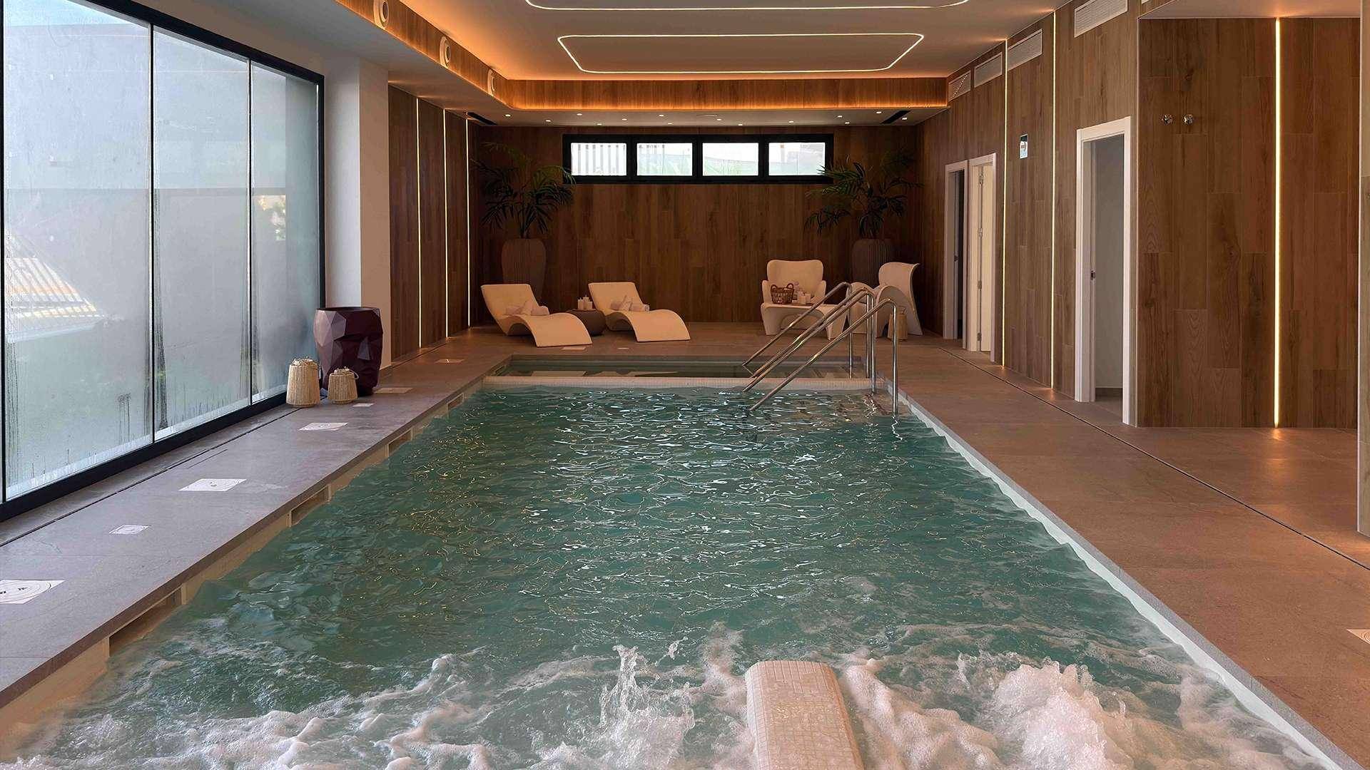 Geräumiger Innenpool mit Sprudelfunktion und Liegebereichen in einem eleganten Wellnessbereich.