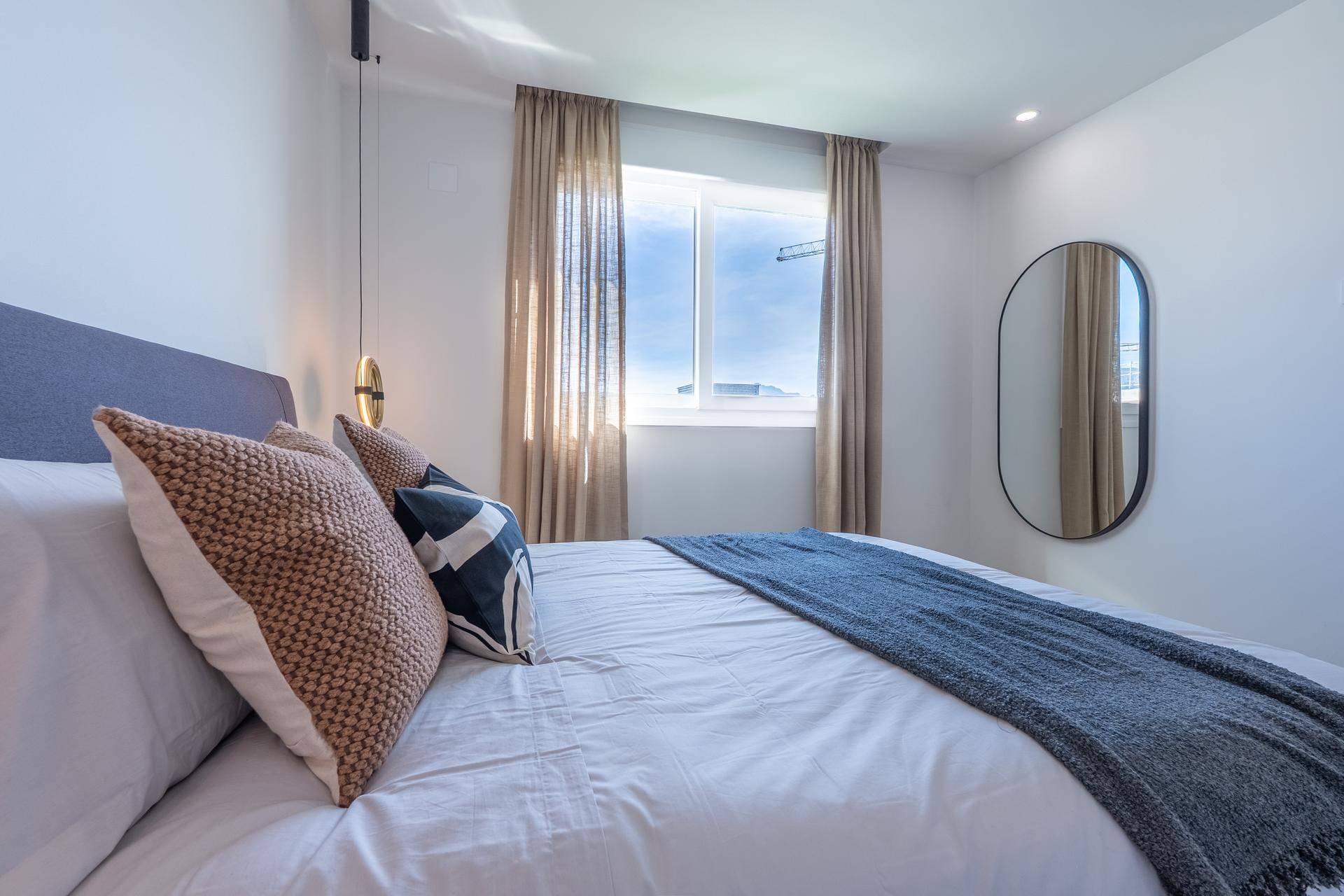 Helles Schlafzimmer mit Doppelbett, Holzboden und Fenster mit Vorhängen.