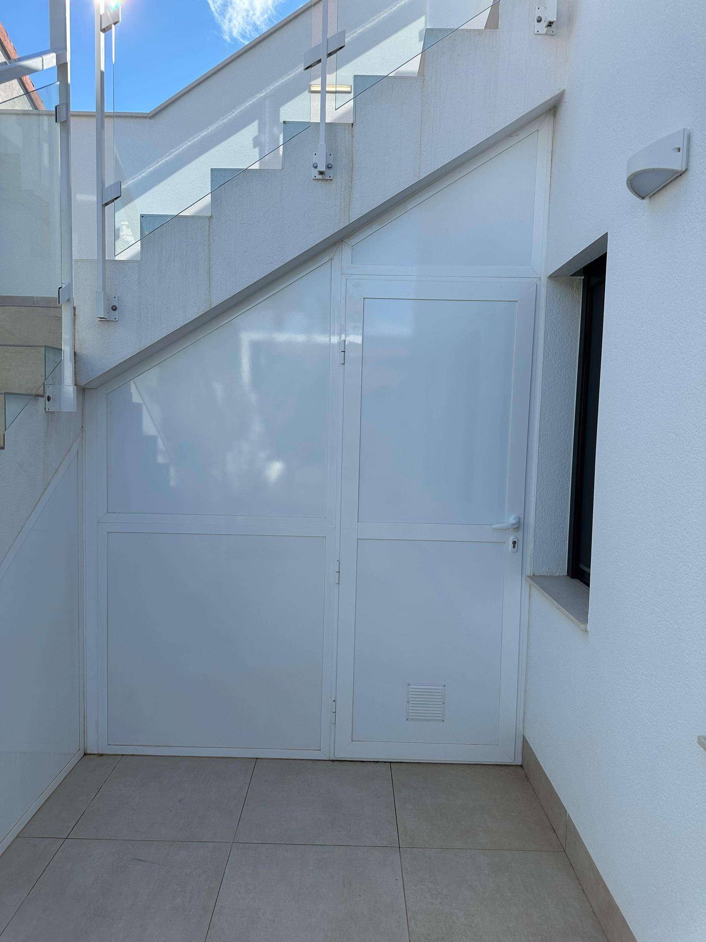 Abstellraum unter der Außentreppe mit weißer Tür und Fenster.