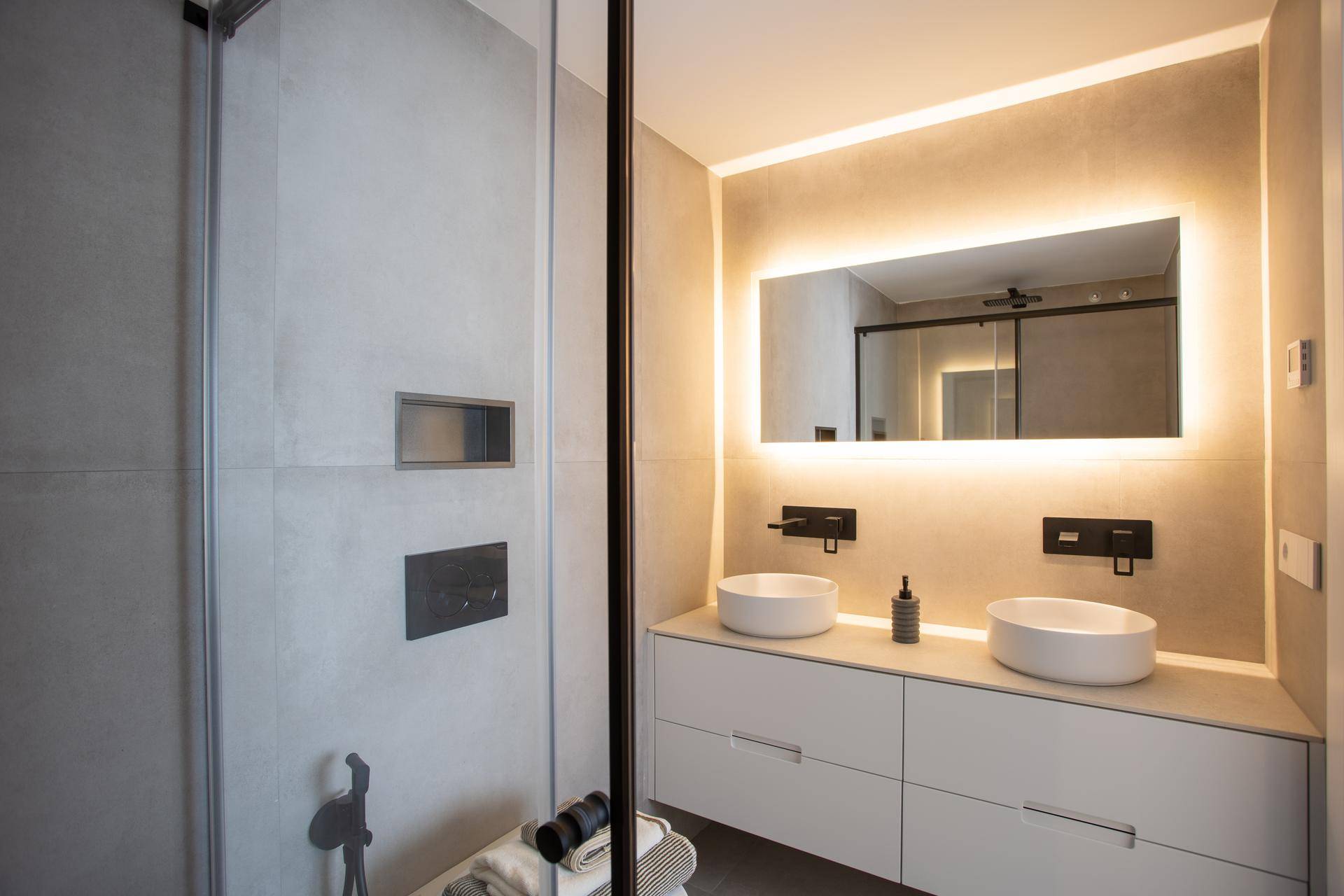 Modernes Badezimmer mit Doppelwaschbecken, beleuchtetem Spiegel und großer Duschkabine.