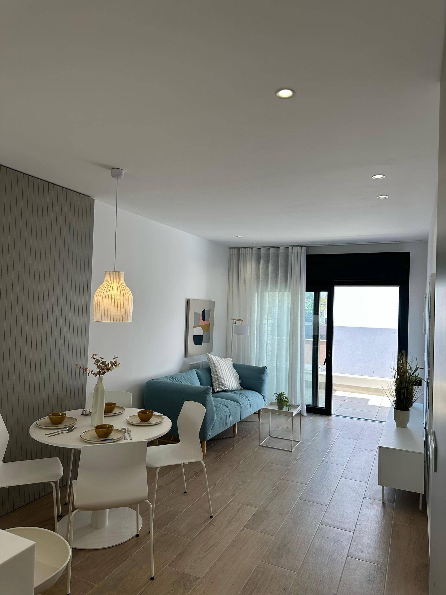 Gemütlicher Wohnbereich mit blauem Sofa, Esstisch und viel Tageslicht durch große Fenster.