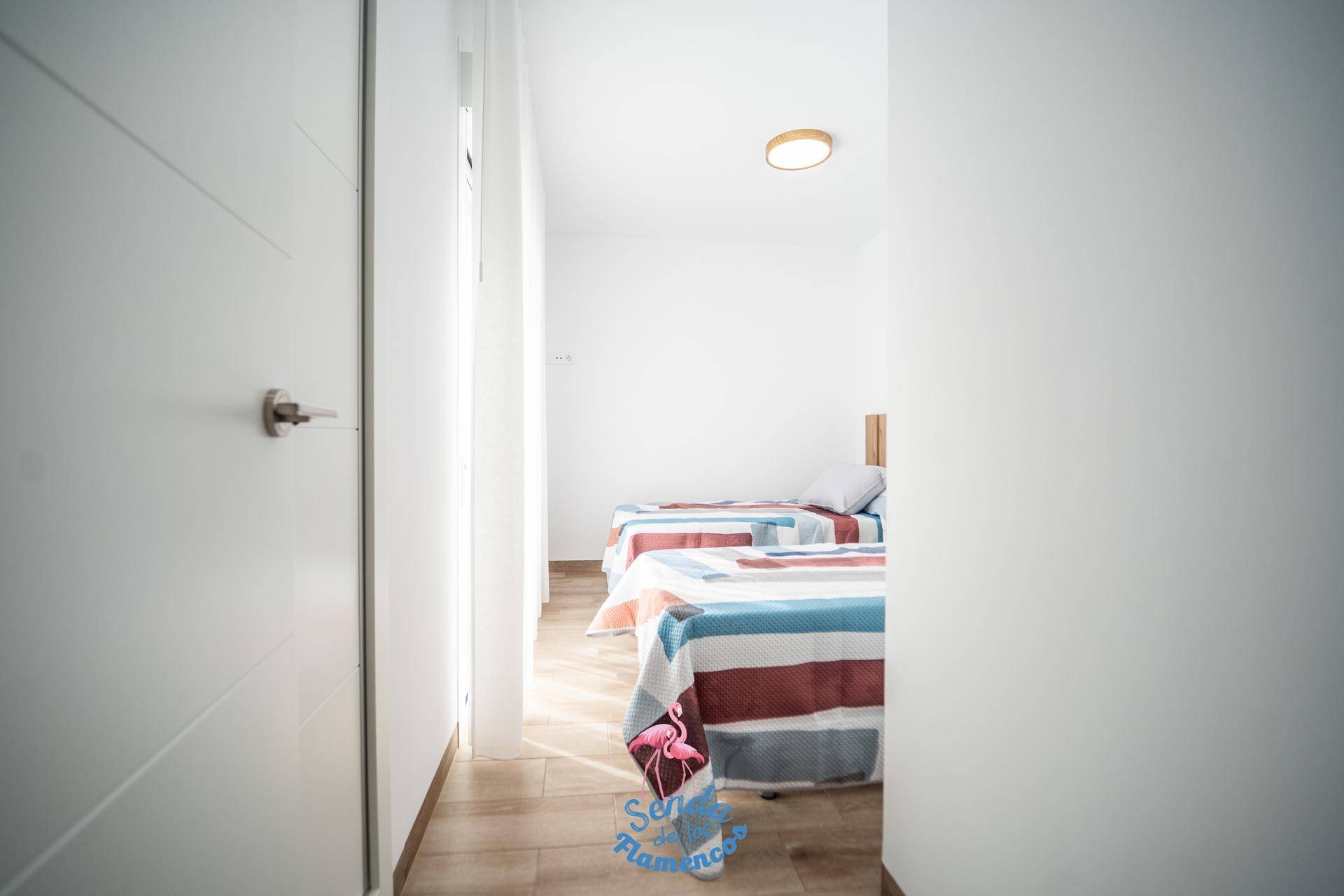 Heller Flur mit Laminatboden, der zu einem Schlafzimmer mit zwei Einzelbetten führt.