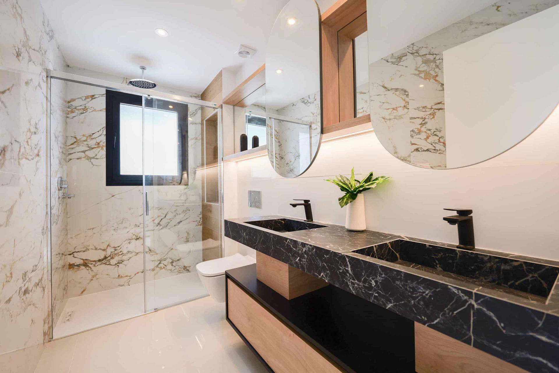 Luxuriöses Badezimmer mit Doppelwaschbecken, schwarzer Marmorplatte und großer Dusche.
