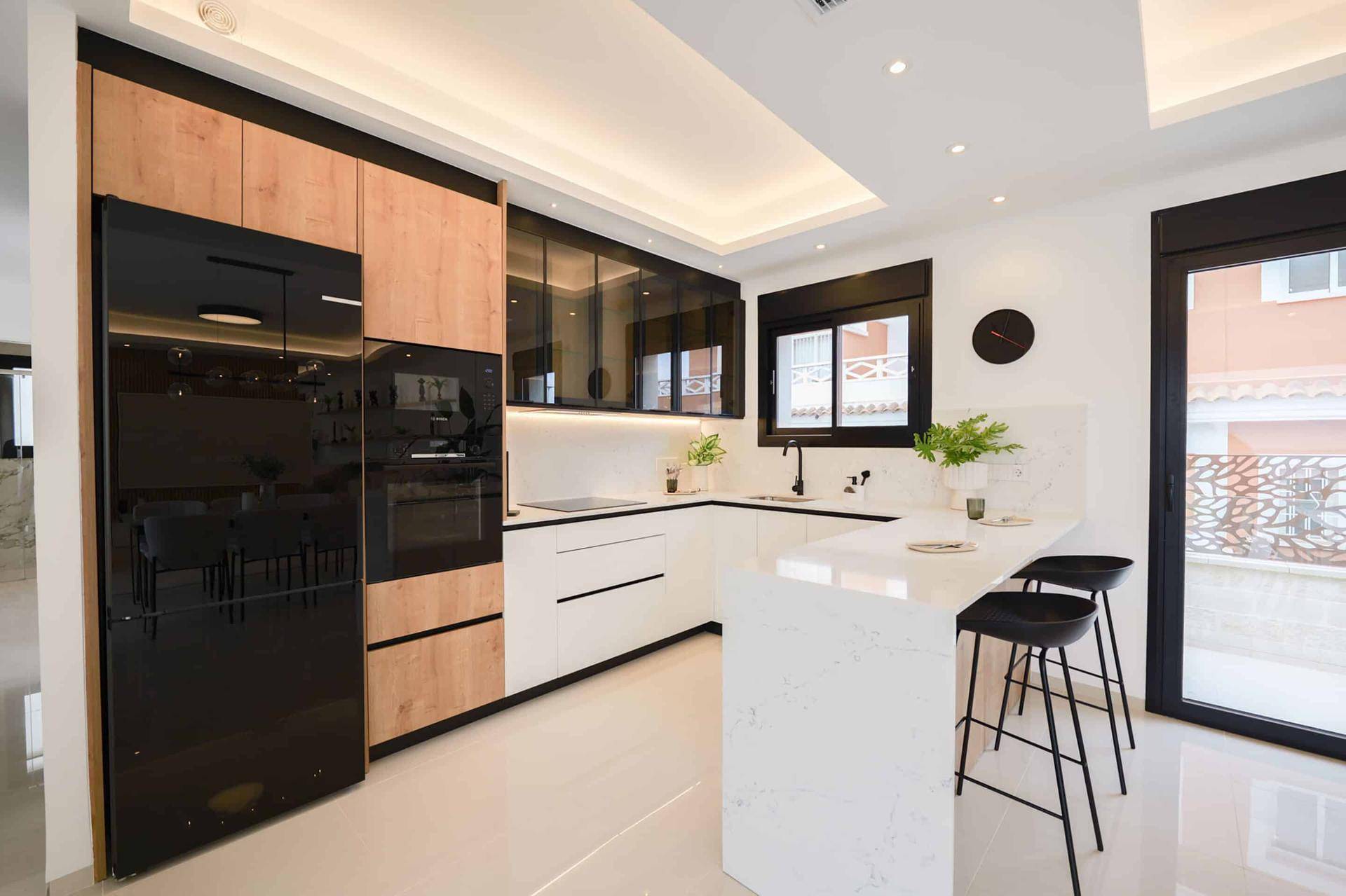Moderne Küche mit schwarzen Geräten, weißer Arbeitsplatte und Frühstücksbar.
