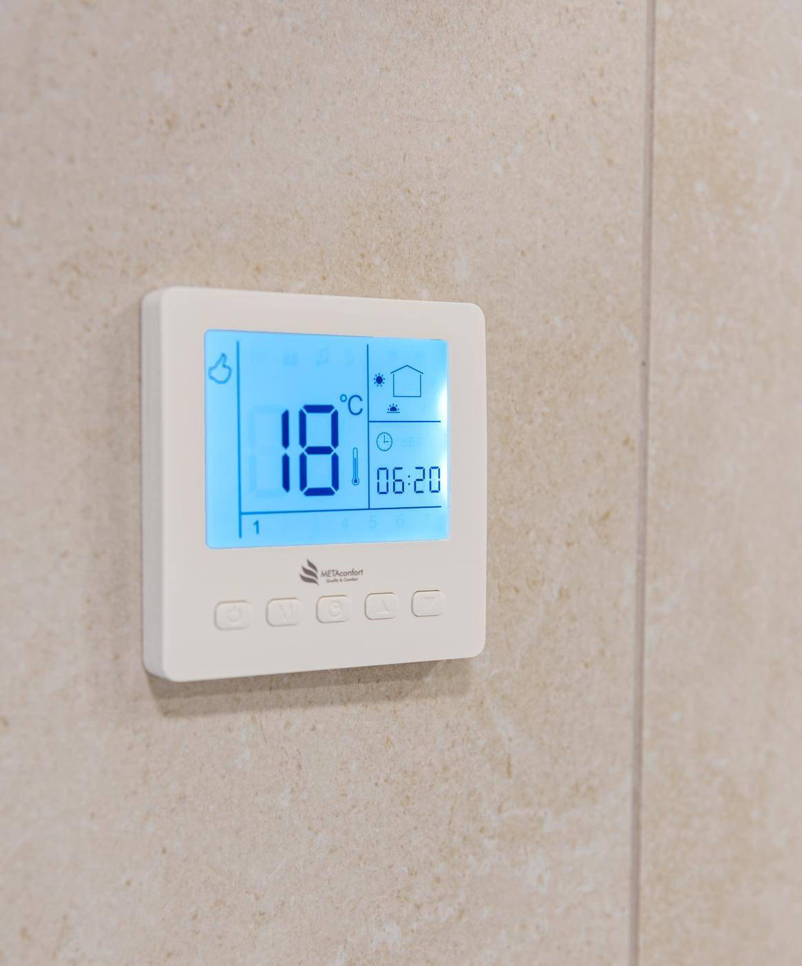 Digitaler Thermostat zur Steuerung der Raumtemperatur, an einer hellen Wand montiert.