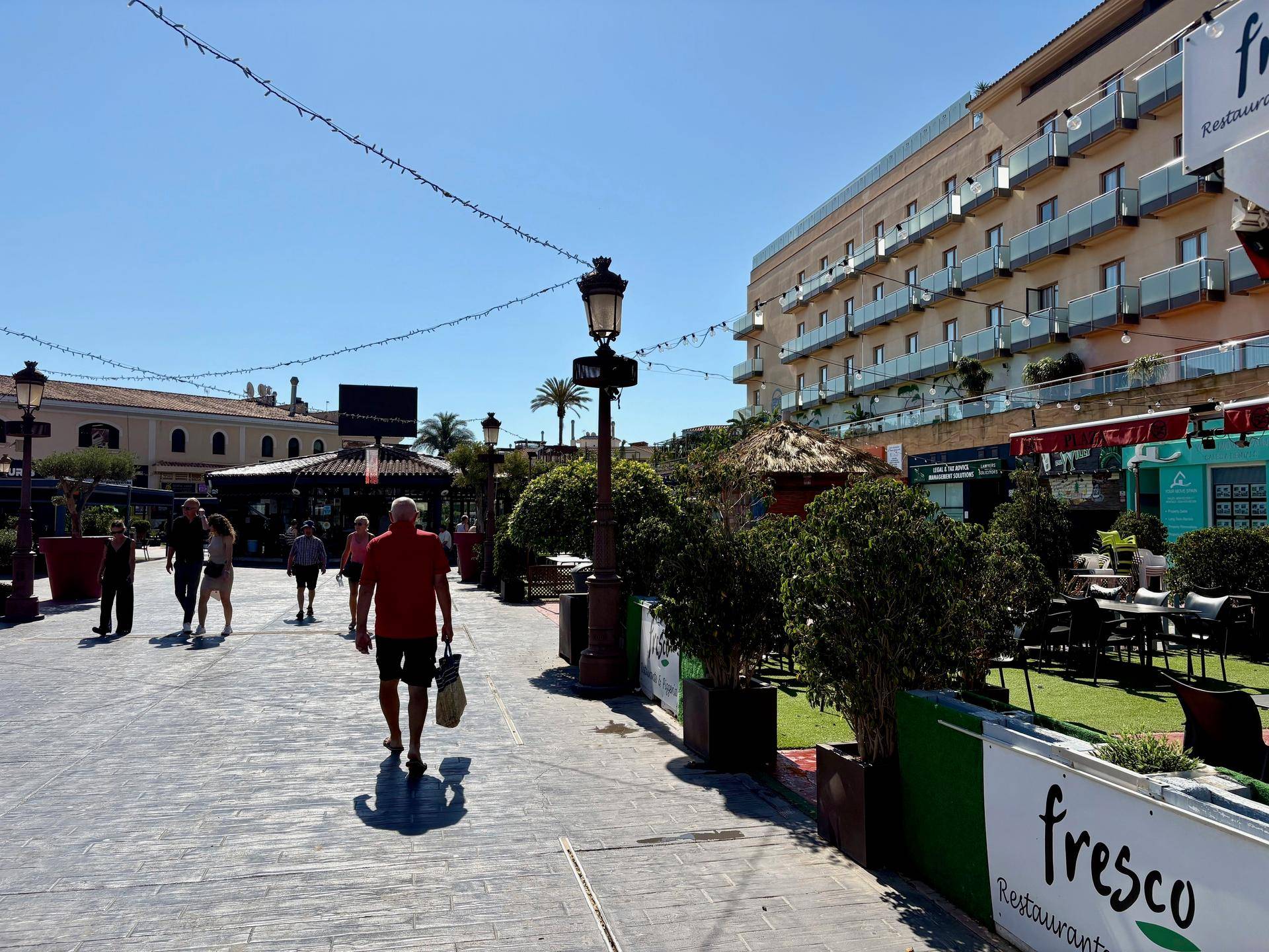 Belebte Promenade mit Restaurants, Geschäften und Menschen, die das sonnige Wetter genießen.