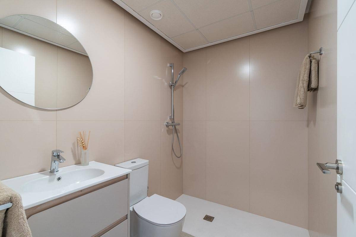 Modernes Badezimmer mit ebenerdiger Dusche, WC und Waschtisch mit rundem Spiegel.