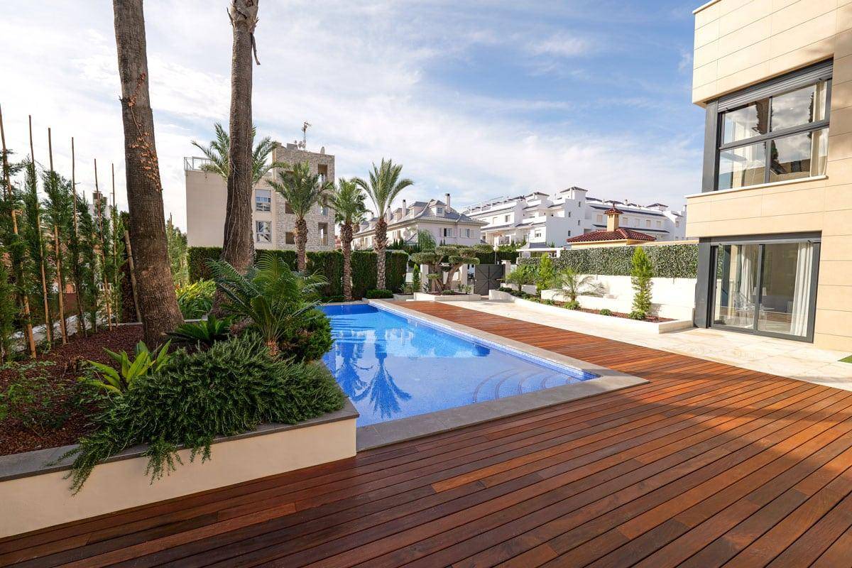 Langer Pool mit Holzdeck und mediterraner Bepflanzung, umgeben von modernen Gebäuden.