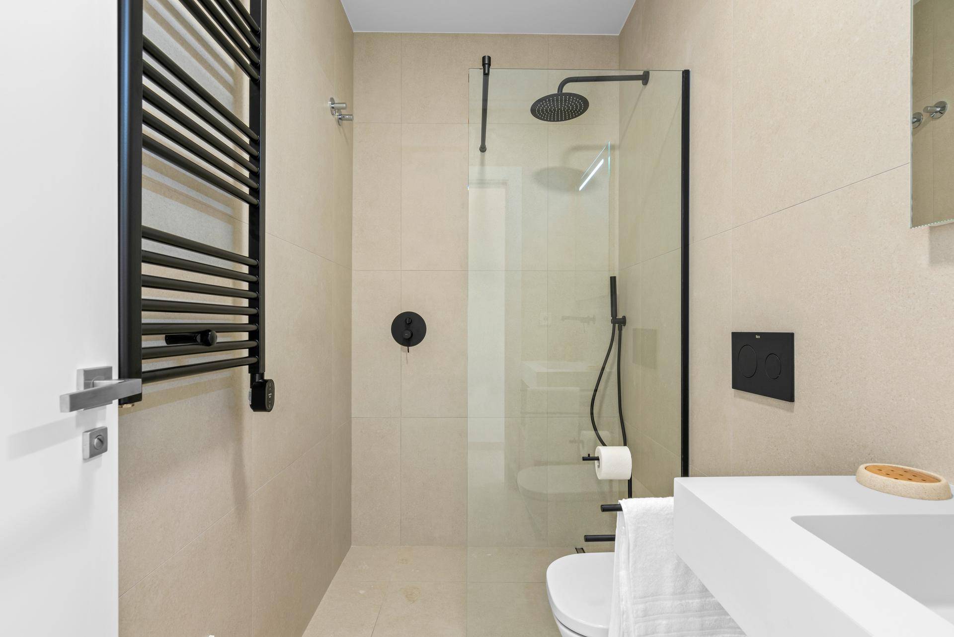 Modernes Badezimmer mit begehbarer Dusche, schwarzer Armatur und beheiztem Handtuchhalter.