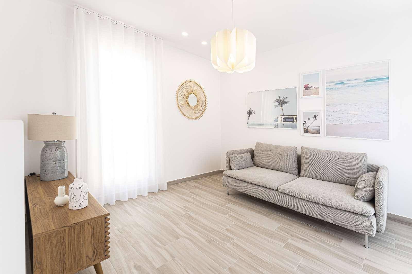 Gemütliches Wohnzimmer mit hellem Sofa, Holztisch und maritimen Bildern an der Wand.