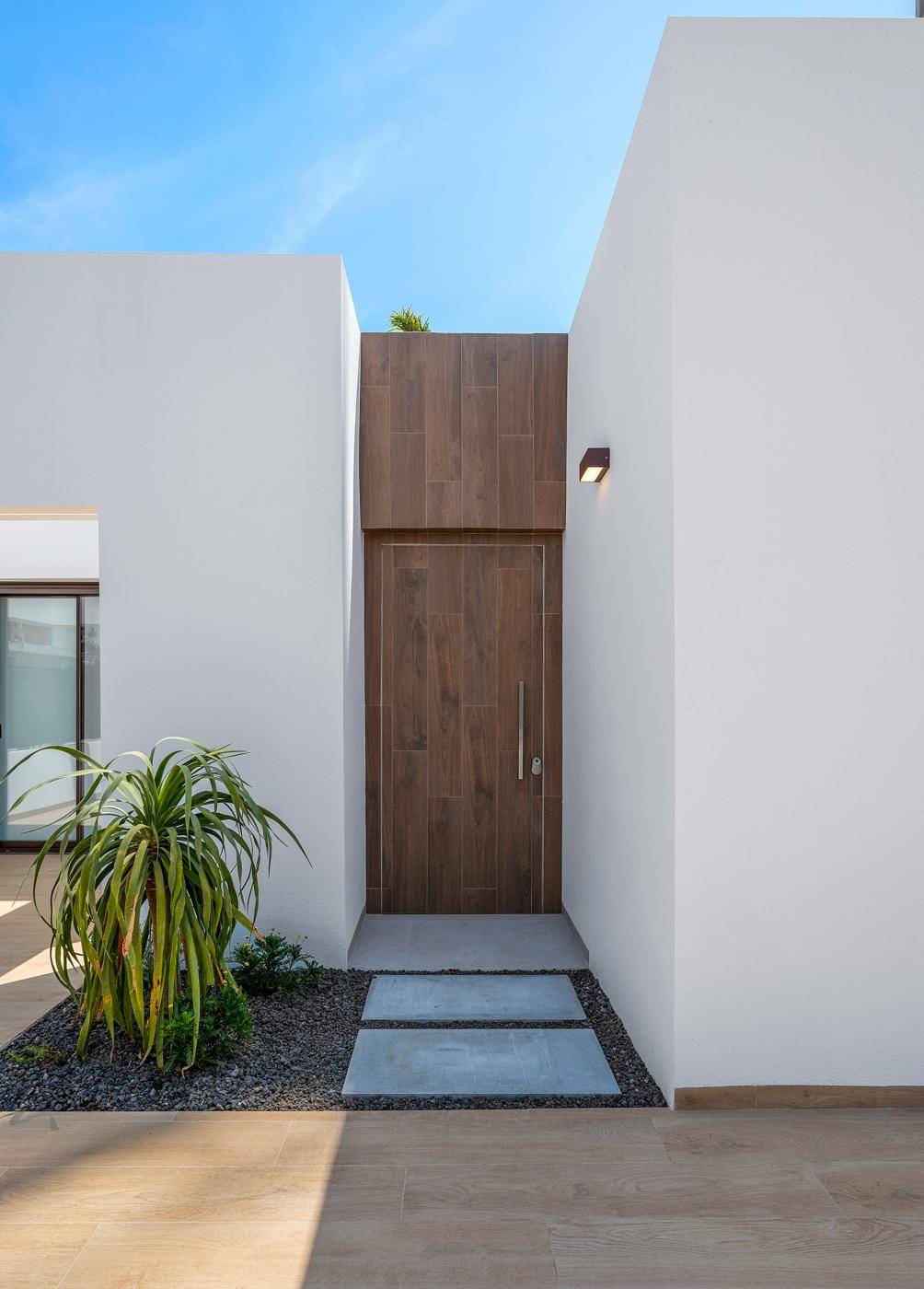 Elegante Eingangstür aus Holz, umgeben von weißer Fassade und Kiesbeet.