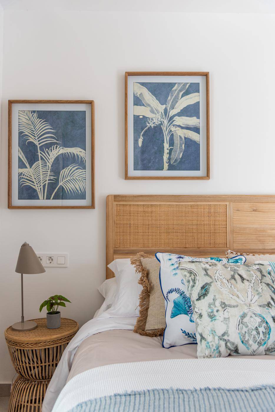 Schlafzimmer mit Rattan-Kopfteil, passenden Nachttischen und maritimen Bildern.