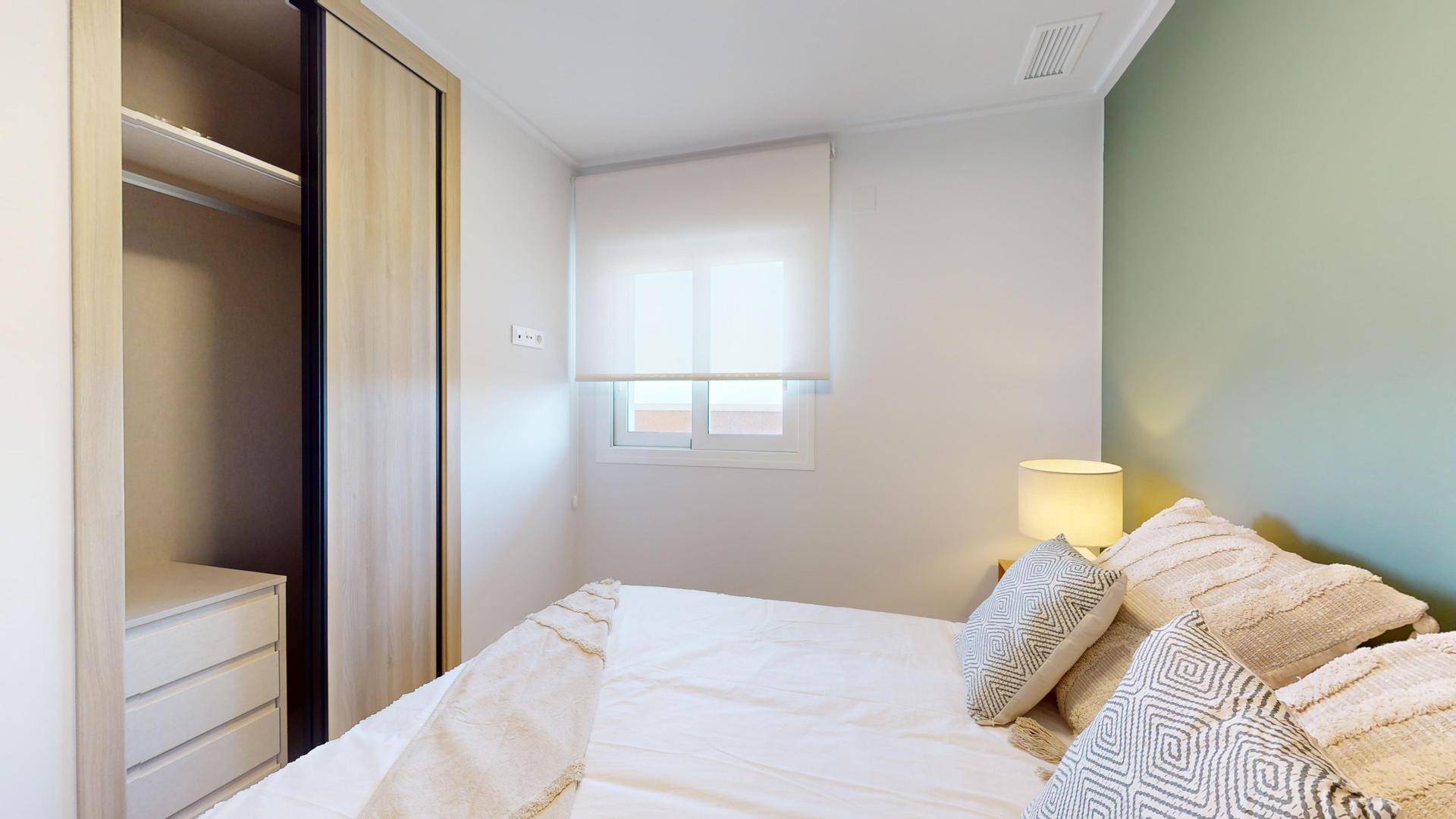 Helles Schlafzimmer mit Doppelbett, Einbauschrank und Fenster für natürliches Licht.