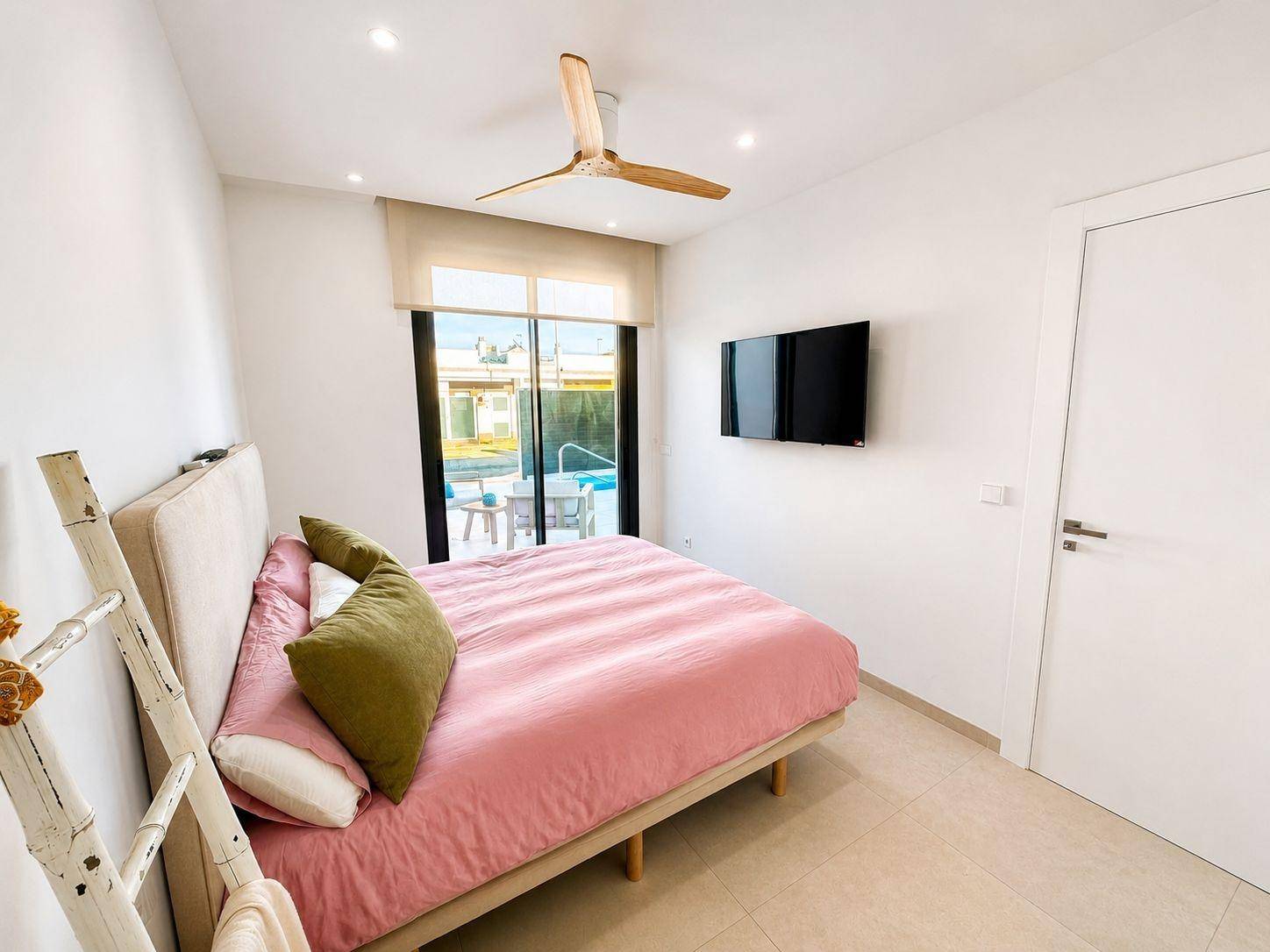 Modernes Schlafzimmer mit Doppelbett, Deckenventilator und Zugang zur Außenterrasse.