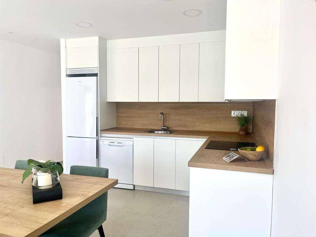 Moderne Einbauküche mit weißen Schränken, Holz-Arbeitsplatte und integrierten Geräten.