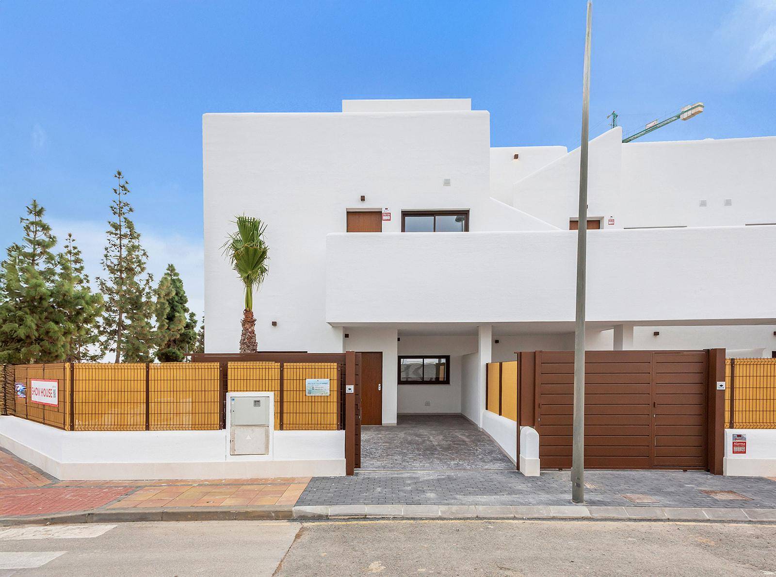 Moderne Hausfassade mit Einfahrt, Zaun und Zugang zum überdachten Parkplatz.