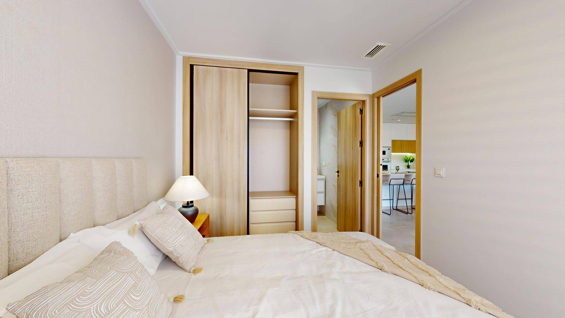 Helles Schlafzimmer mit Doppelbett und integriertem Holzschrank, Zugang zu Bad und Küche.