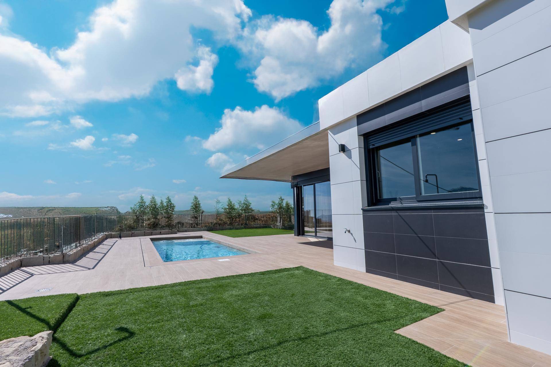 Seitlicher Blick auf die moderne Villa mit Poolbereich, Kunstrasen und weitem Ausblick.
