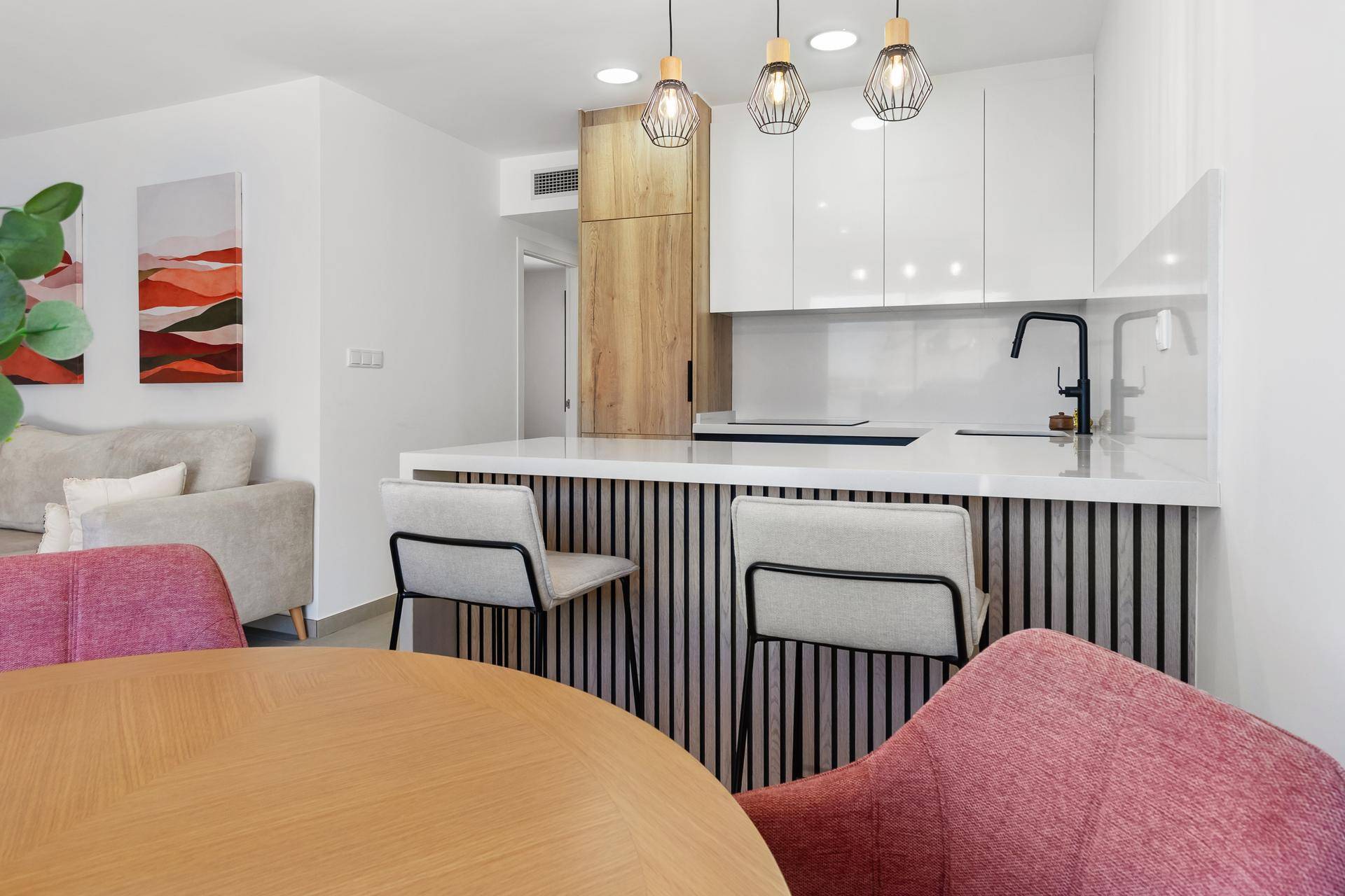 Moderner Essbereich mit Holztisch, rosa Stühlen und offener Küche mit Frühstücksbar.