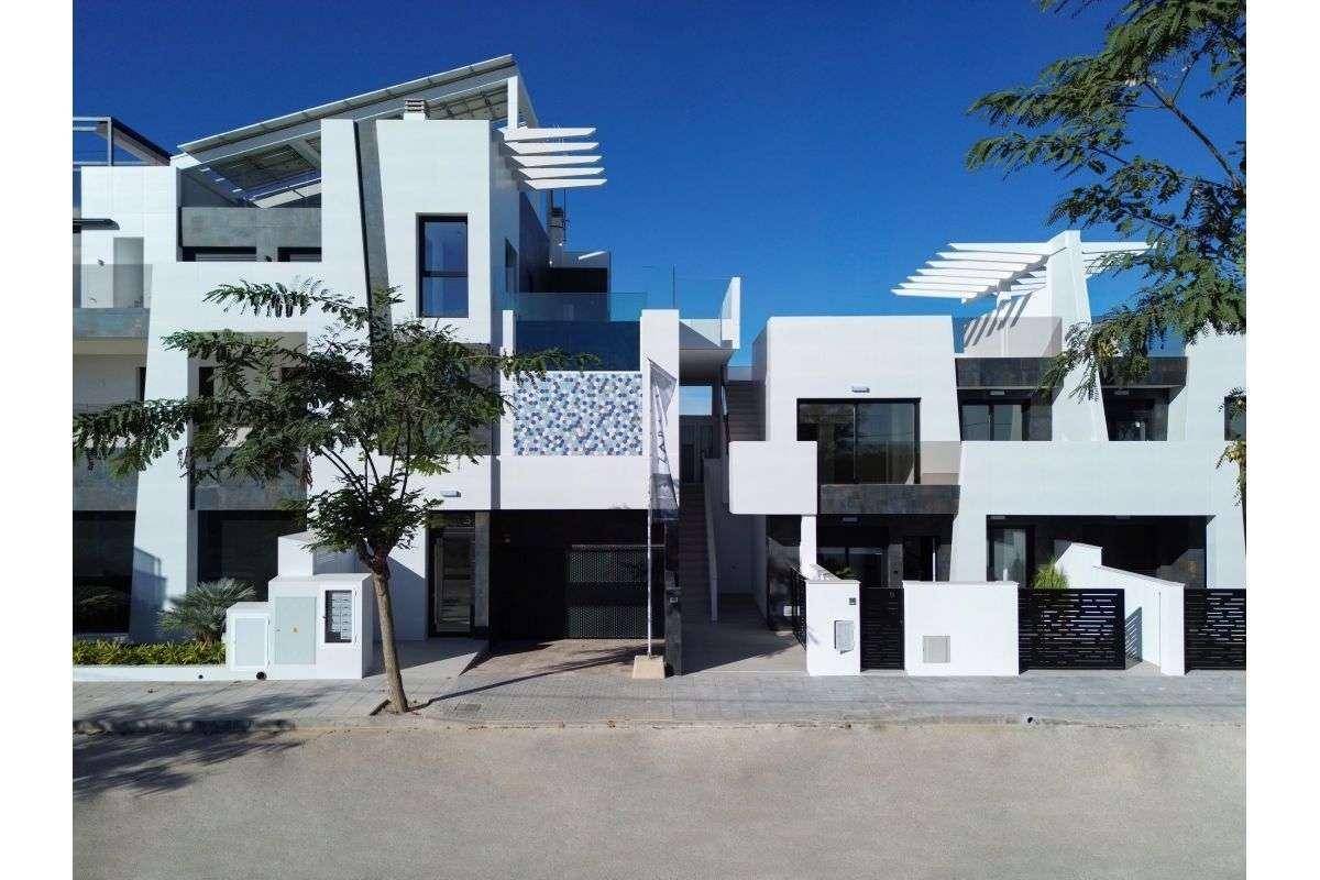 Moderne Wohnanlage mit weißer Fassade, großen Fenstern und dekorativen Elementen an einem sonnigen Tag.