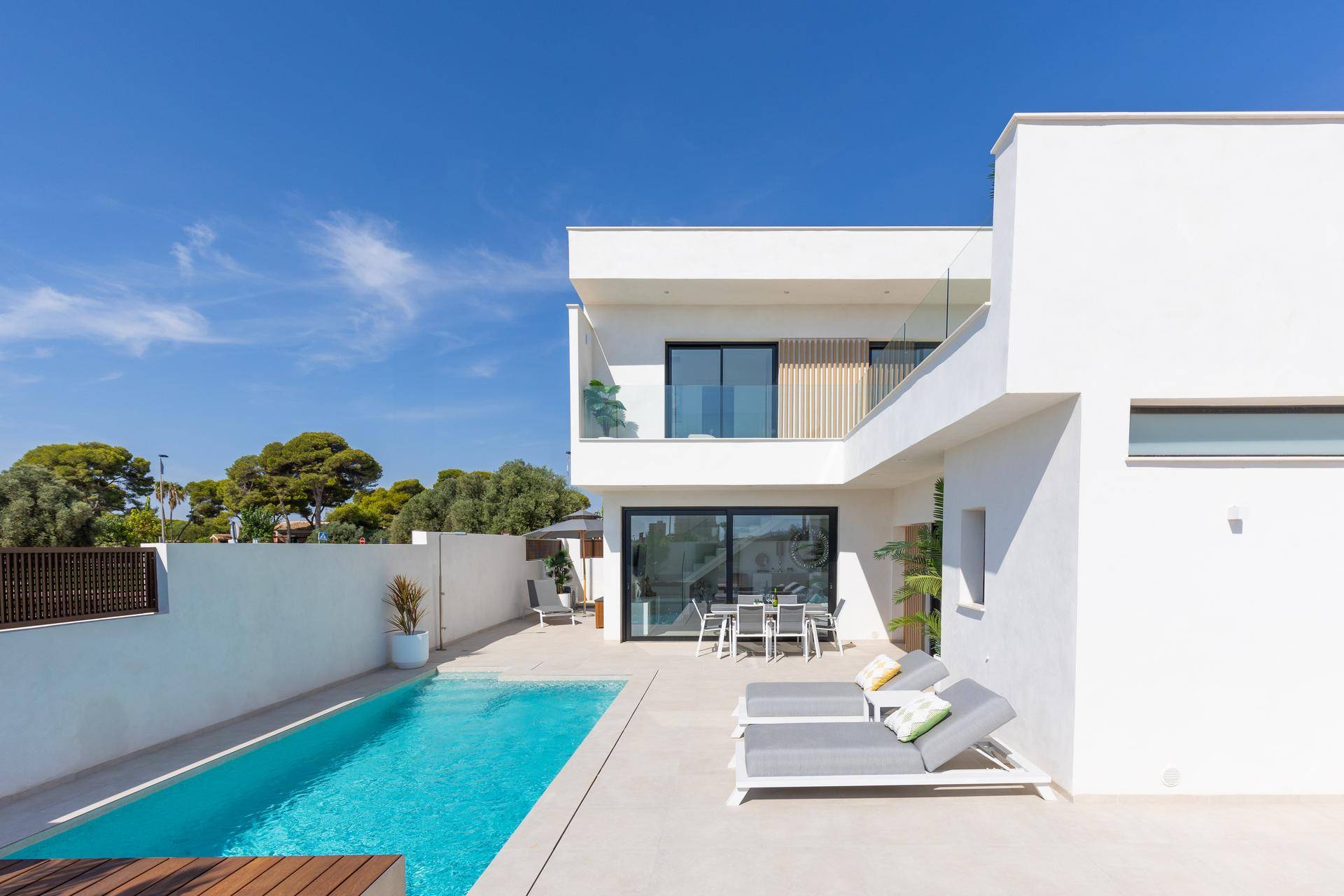 Moderne Villa mit langem Pool und sonniger Terrasse, umgeben von einer niedrigen Mauer.