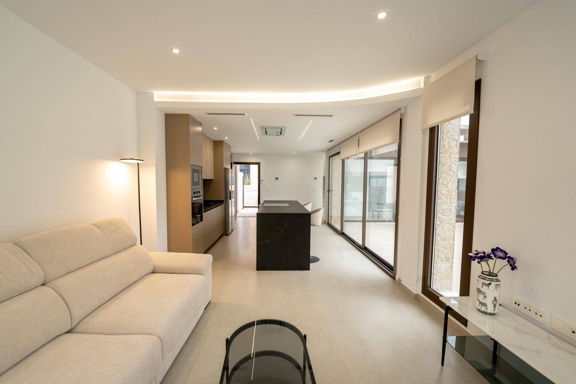 Offener Wohnbereich mit beigem Sofa und moderner Küche im Hintergrund, mit Zugang zur Terrasse.