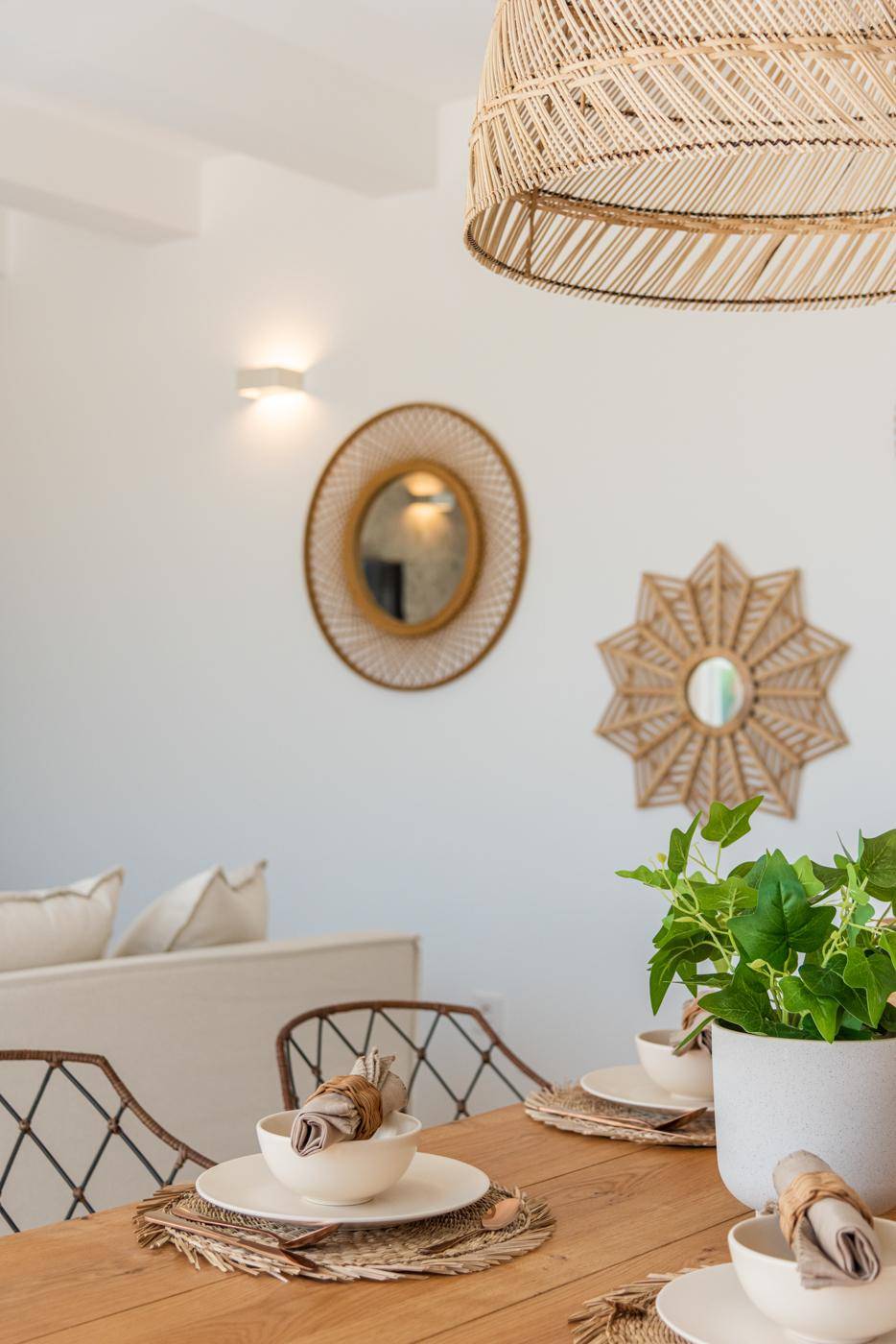 Detail des Essbereichs mit Holztisch, Rattan-Stühlen und dekorativen Spiegeln an der Wand.