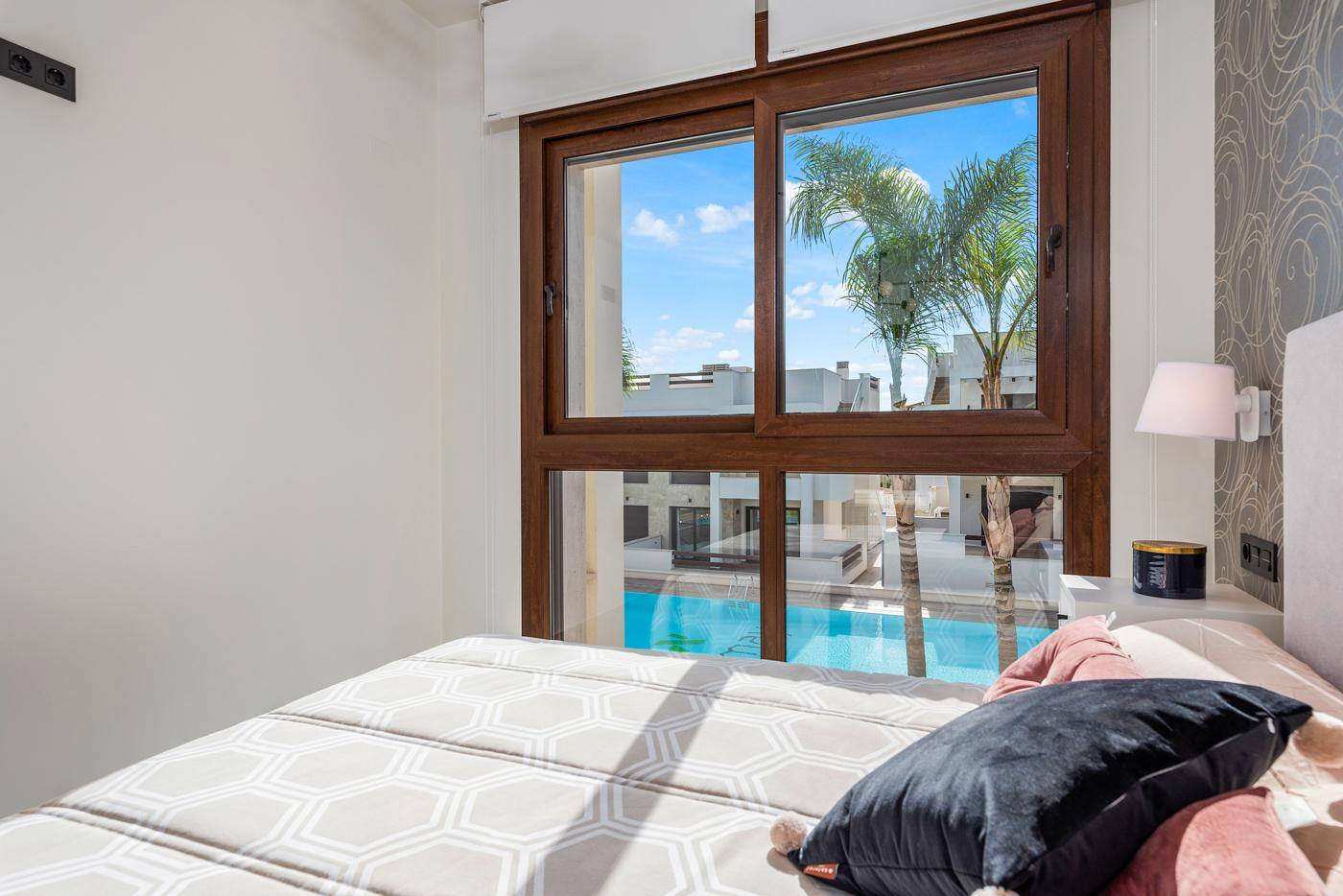 Fenster im Schlafzimmer mit direktem Blick auf den Gemeinschaftspool und die tropischen Palmen.