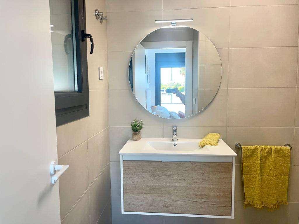 Modernes Badezimmer mit Einzelwaschbecken, rundem Spiegel und Fenster für Belüftung.