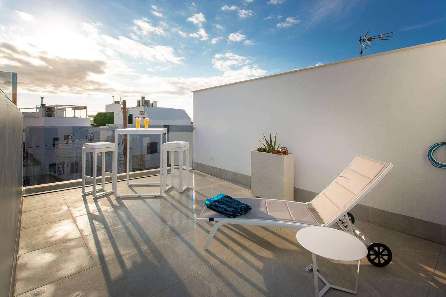 Geräumige Dachterrasse mit Sonnenliege, Sitzbereich und weitem Blick auf die umliegende Bebauung.