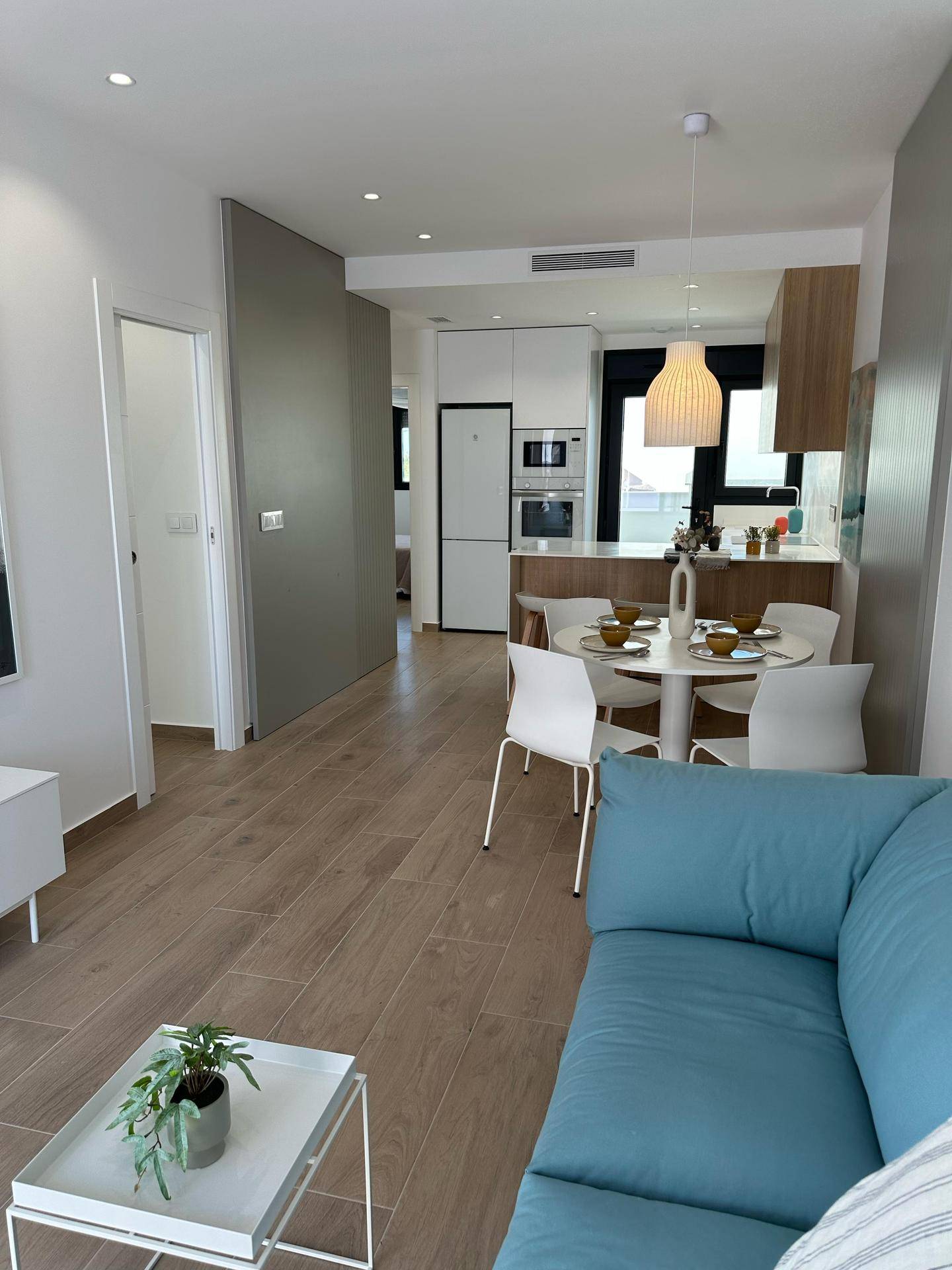 Offener Wohn-Essbereich mit integrierter Küche, blauem Sofa und modernem Fliesenboden in Holzoptik.